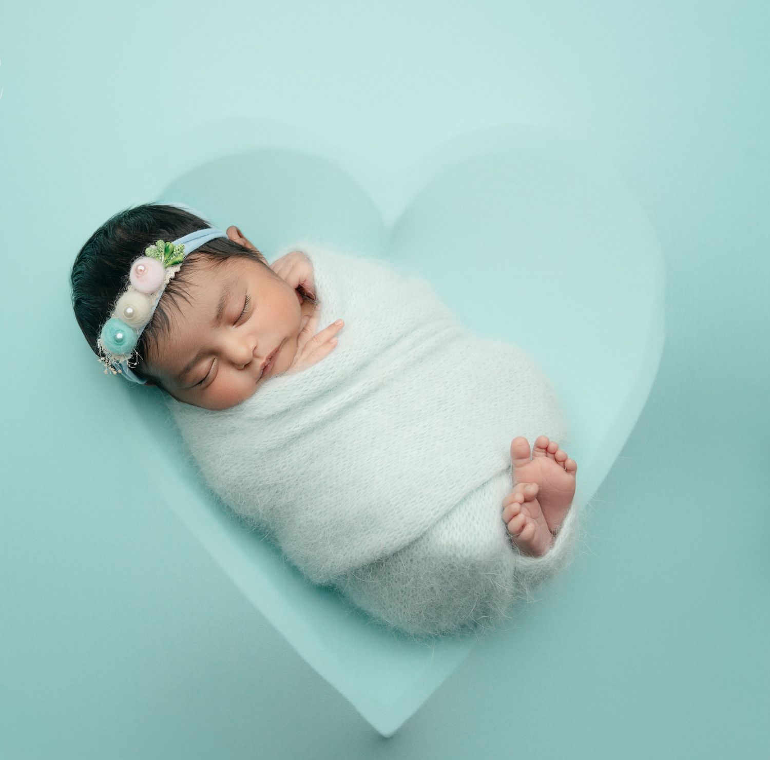 A newborn baby girl is posed in a heart-shaped bowl during her in-home session in Orange County, CA.