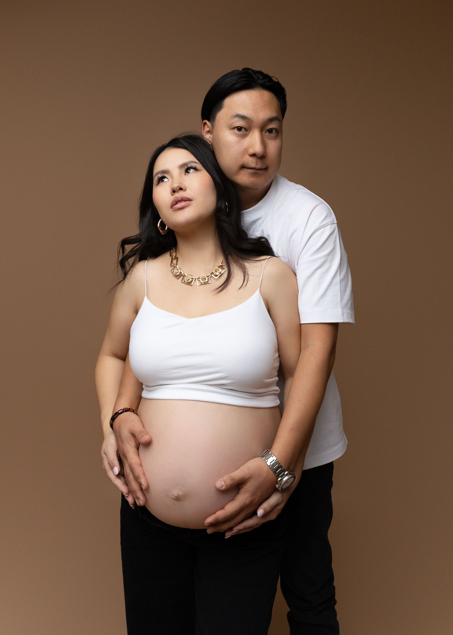 A pregnant woman poses with her partner in the studio during their maternity session.