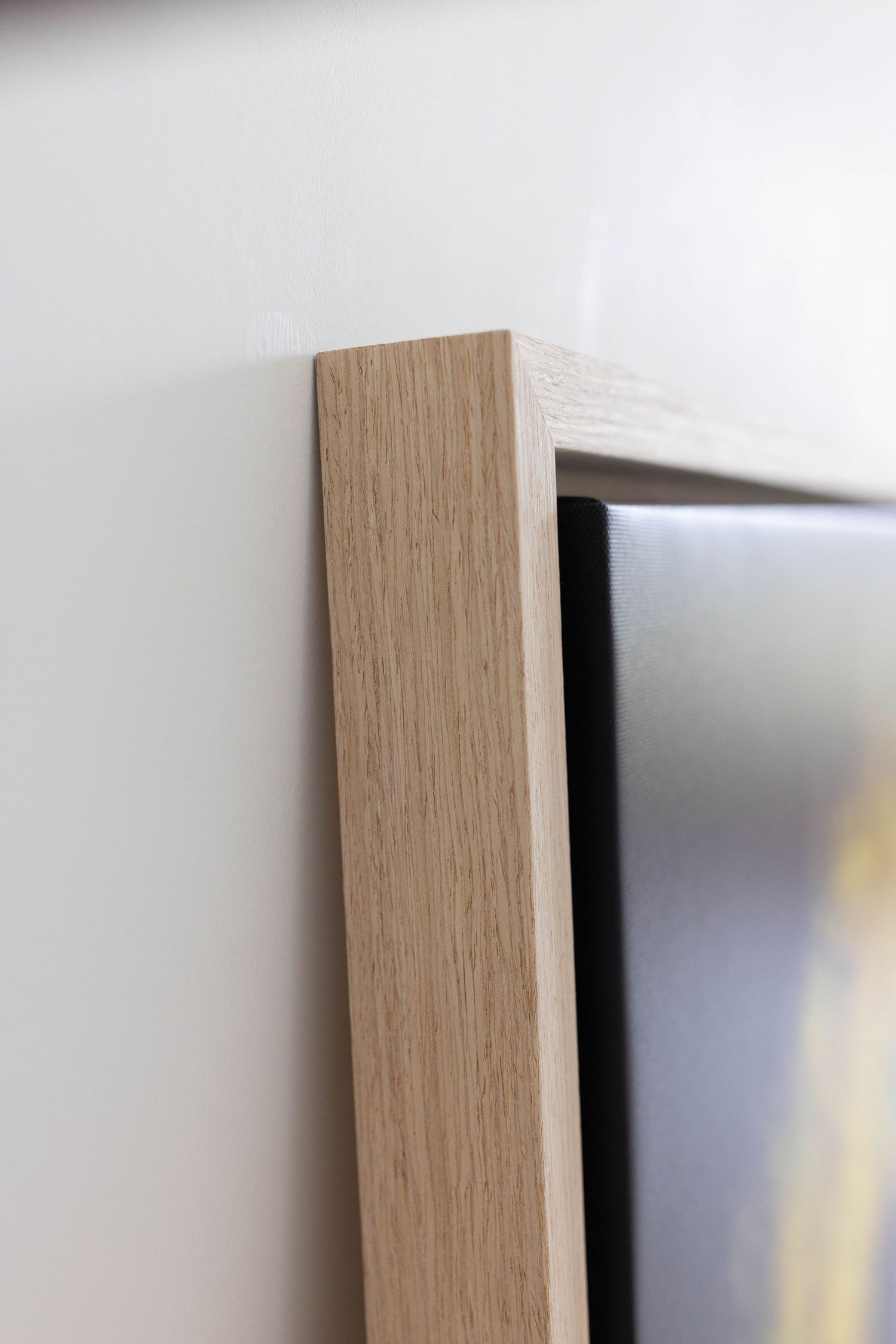 Close-up view of a light wood frame edge detail on a mounted display against a white wall.
