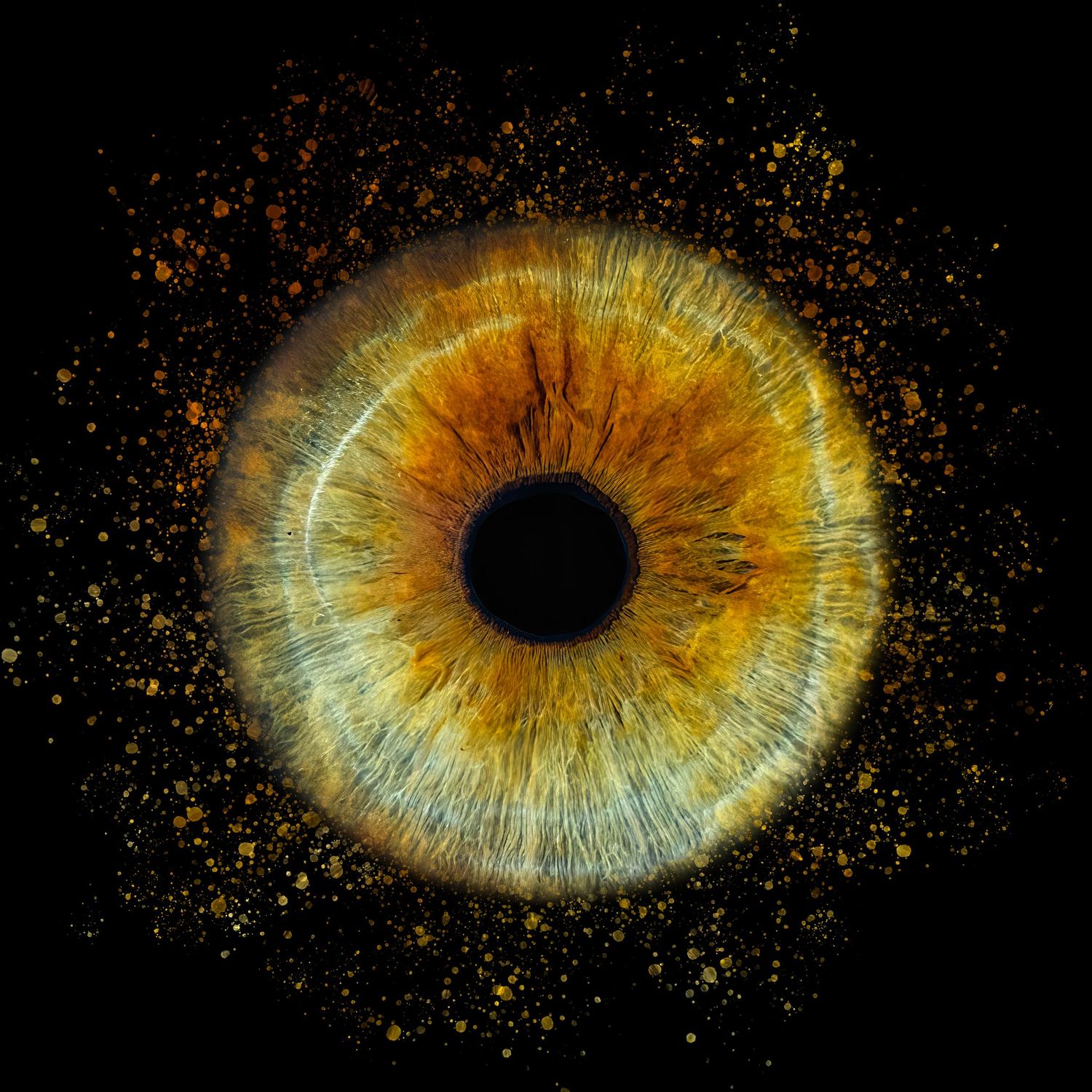 Extreme close-up of an amber-colored human iris with particle effects against dark background.