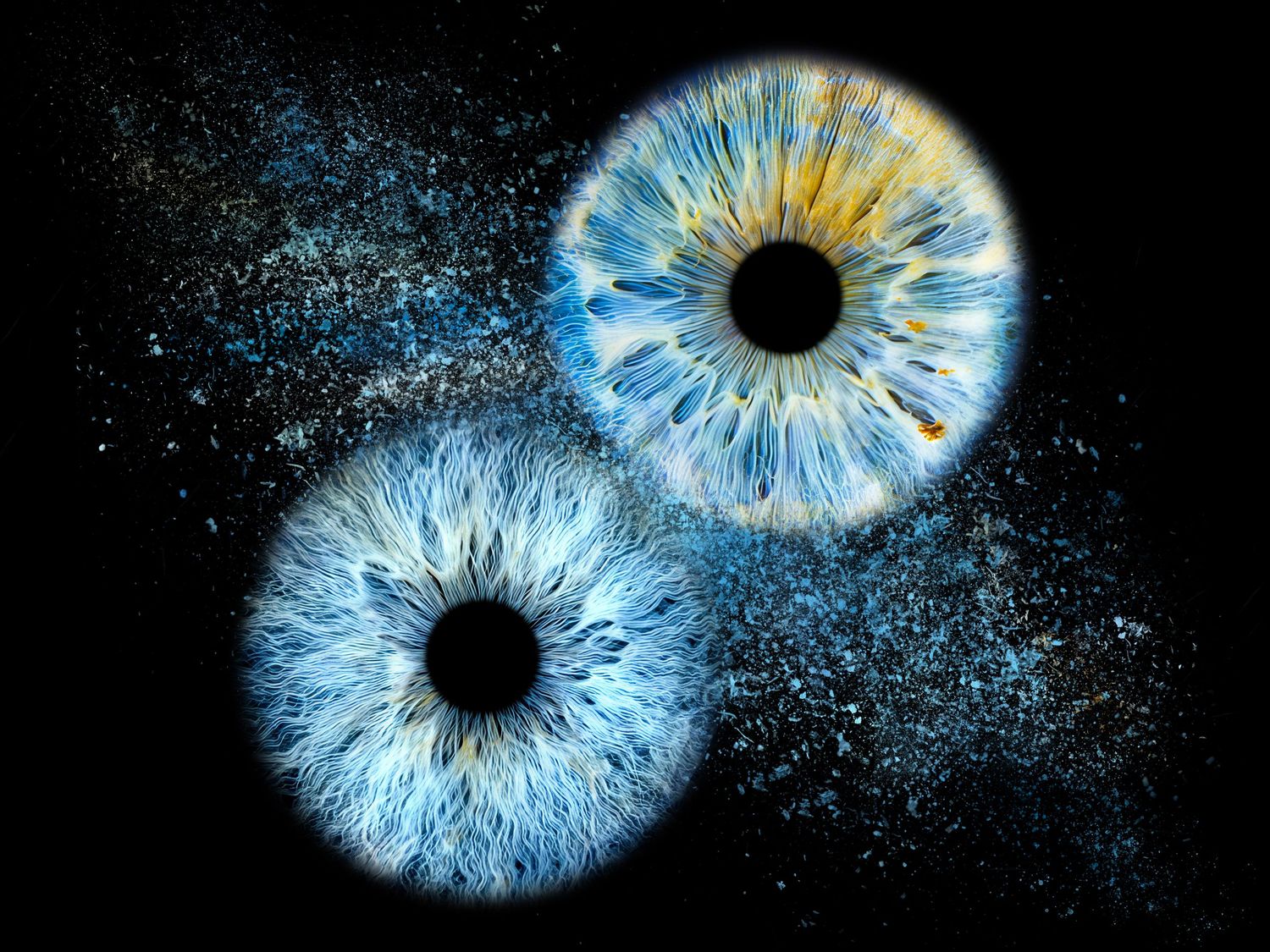 Two macro close-up blue human irises with golden flecks floating on a dark background resembling galaxies.