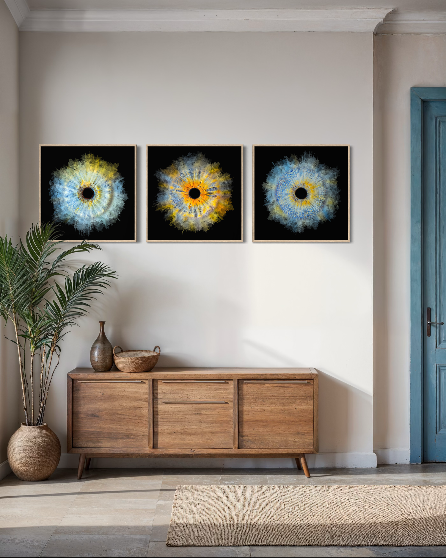 Three framed abstract eye-inspired circular artworks in blue and yellow on black backgrounds displayed above a wooden sideboard.