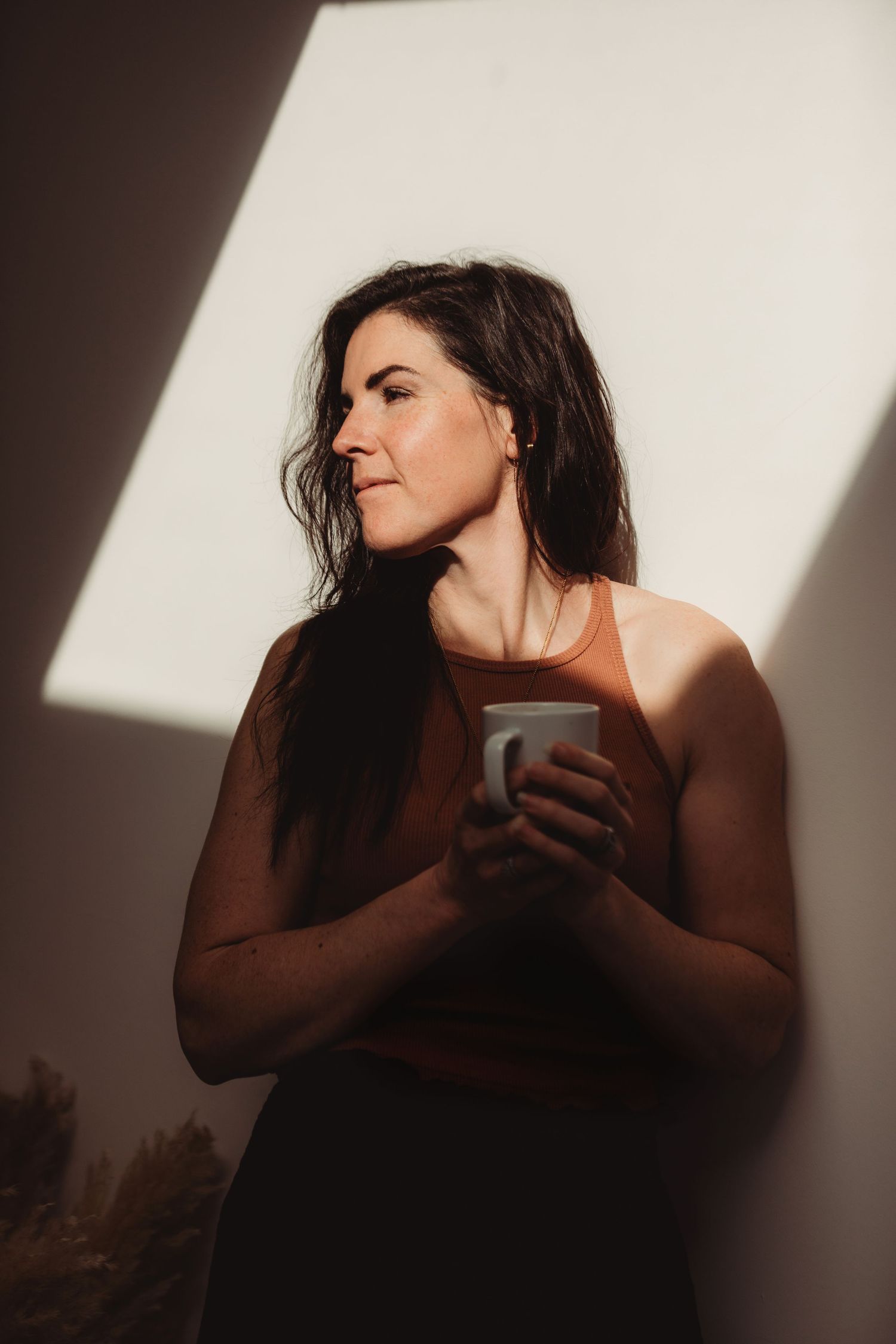 Artistic portrait of a person in dramatic side lighting holding a cup near a white wall.