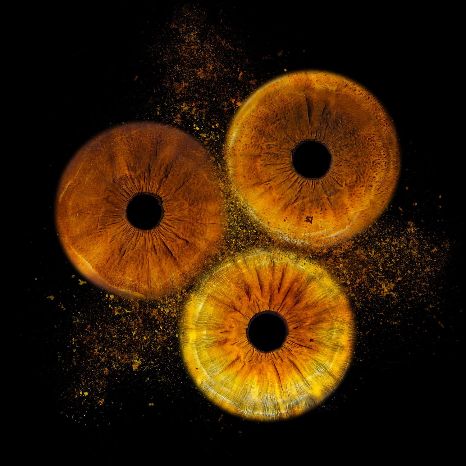 Three golden amber human irises with black pupils on dark background, glowing with orange light and golden particles.