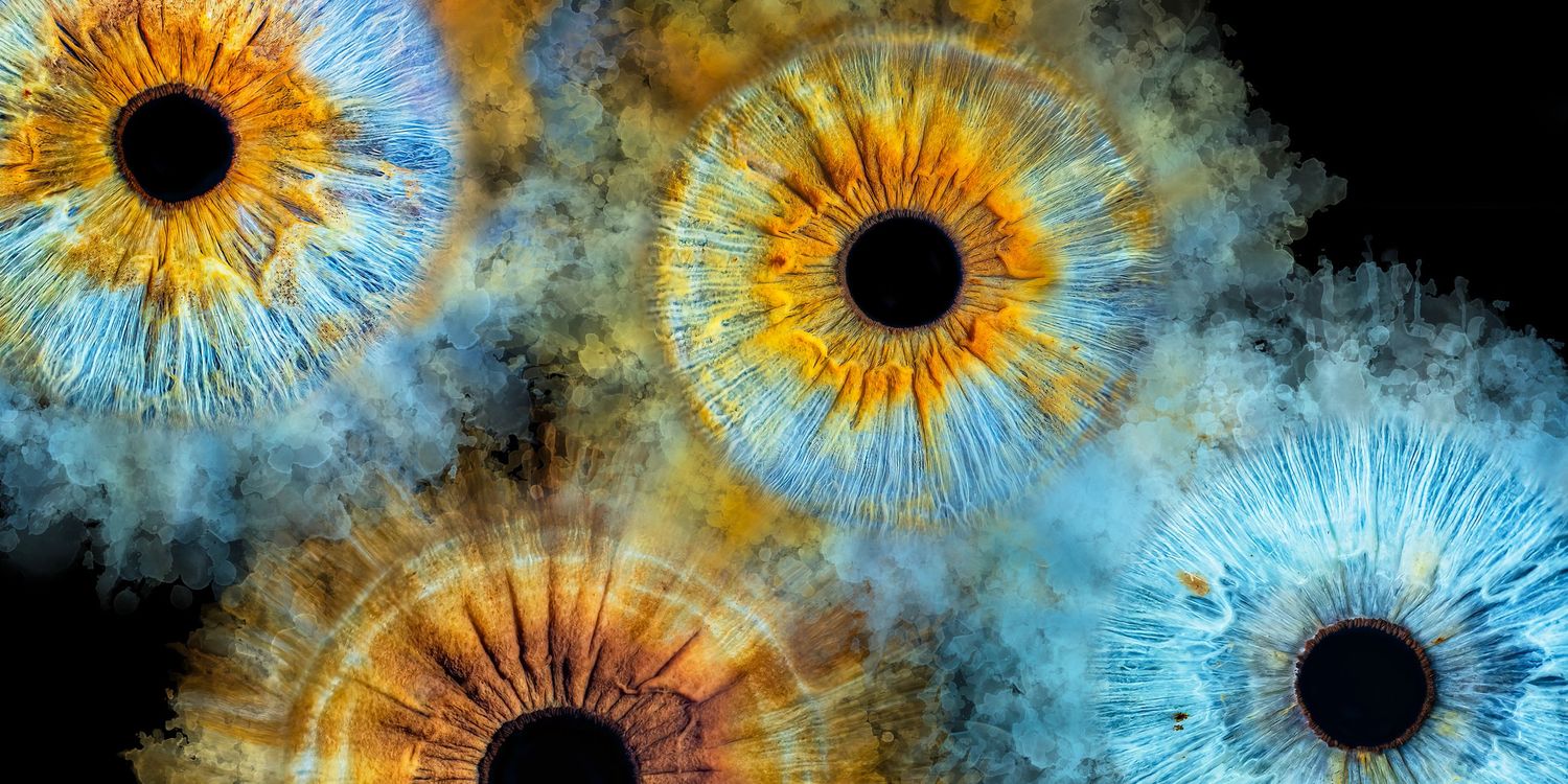 Closeup macro photograph of colorful iris patterns resembling galaxies in blue, orange and gold against black background.