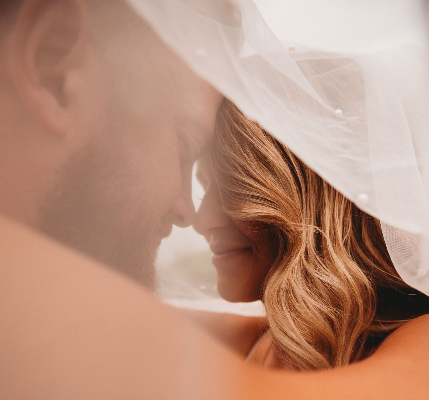 Bride and groom share an intimate moment under a flowing white wedding veil.