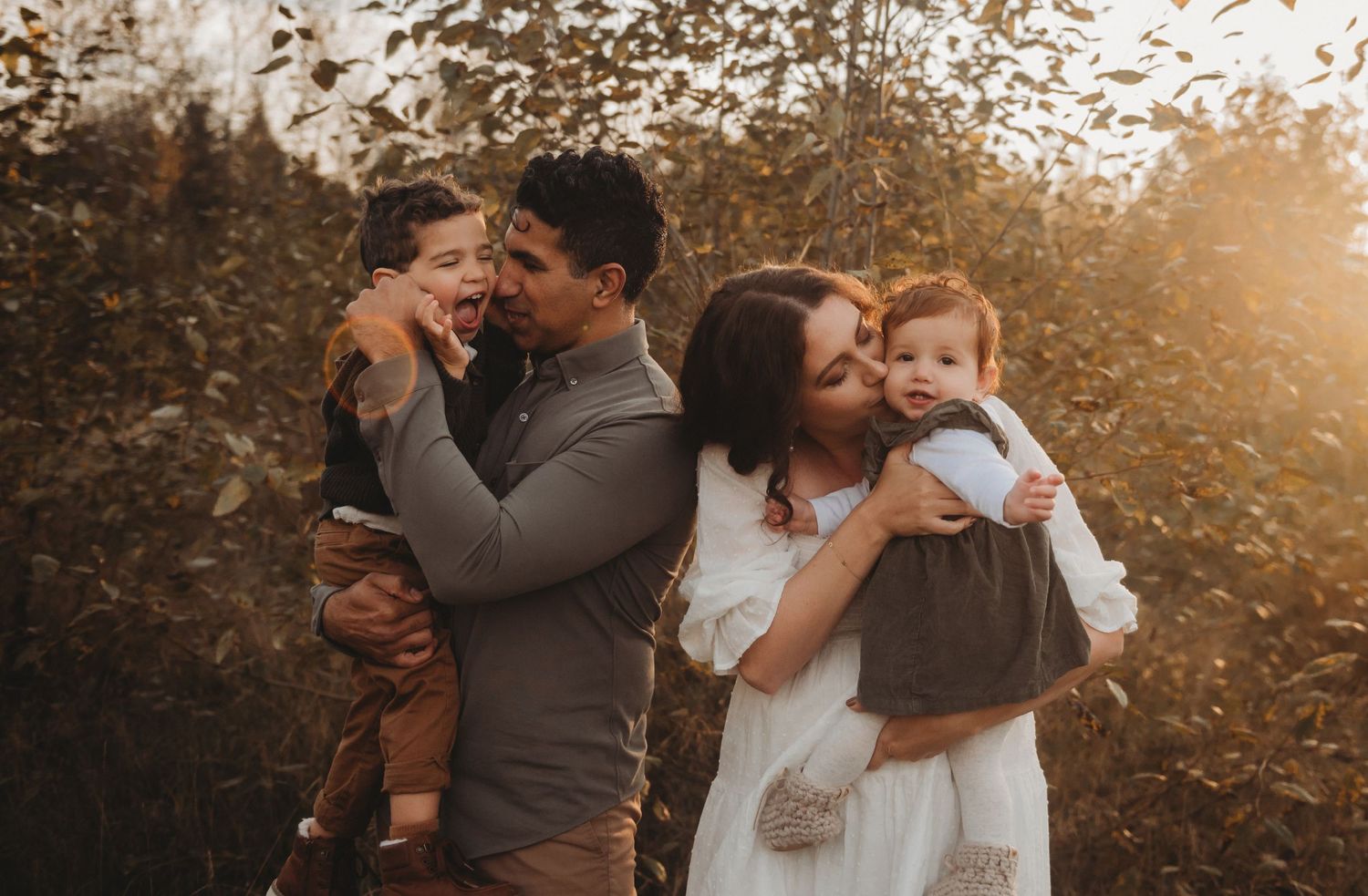 A family of four laughs and plays together in a golden autumn outdoor photo session.