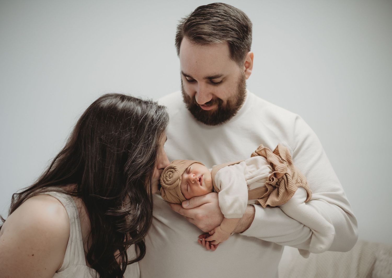 Smiling parents lovingly gazing at their newborn baby during an intimate family photo session.