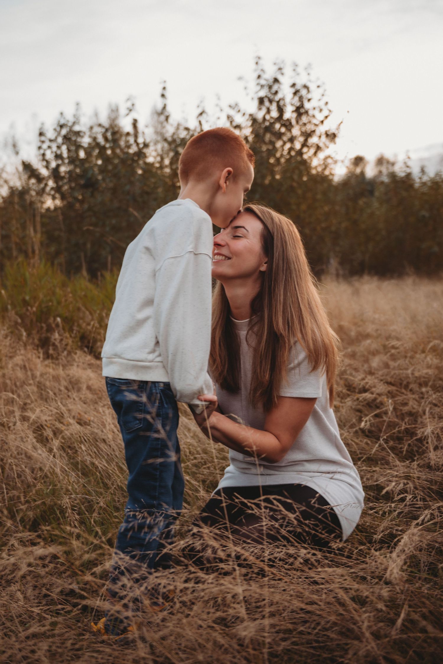 Loving mother and red-haired son sharing a tender forehead kiss in autumn meadow.