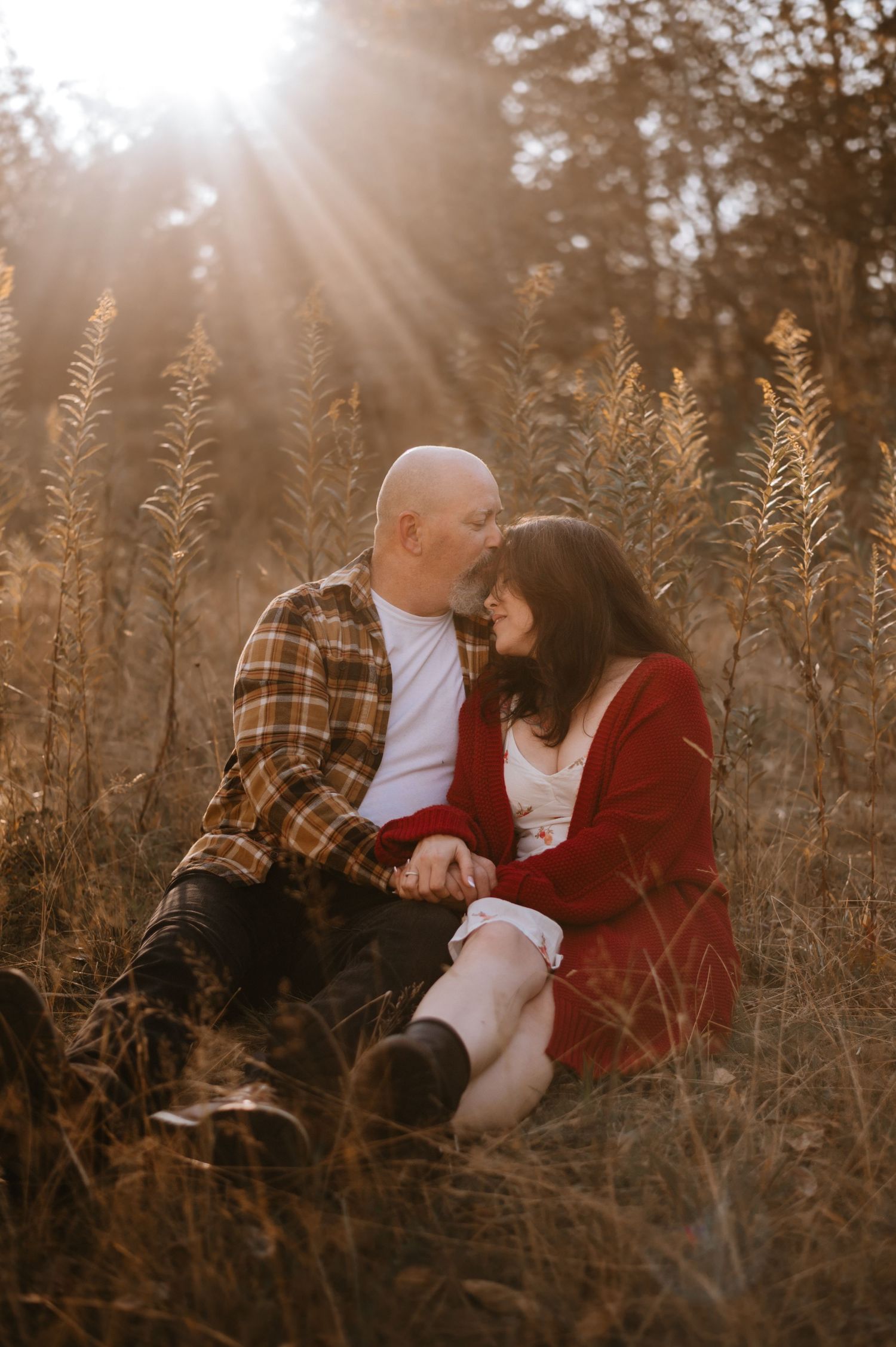 Couple leaning in for a kiss in a golden field with beautiful sun rays behind them.