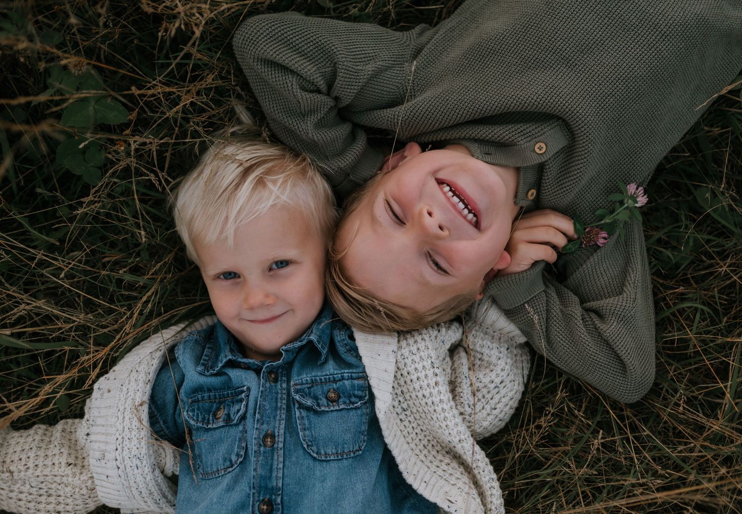 Two young children lying in autumn grass smiling during a golden hour family photo session.