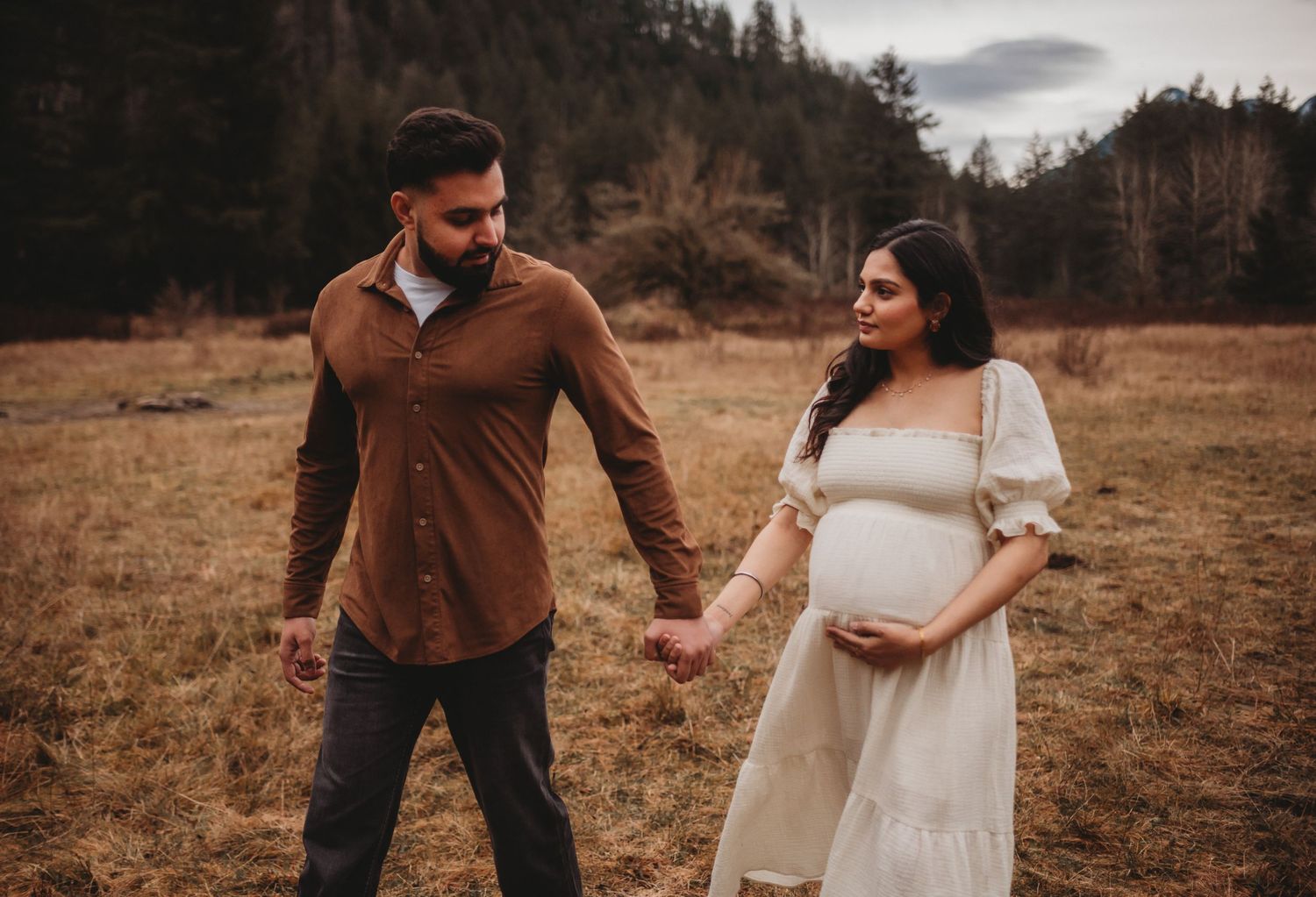 Expecting couple holding hands and gazing at each other in scenic autumn mountain field.