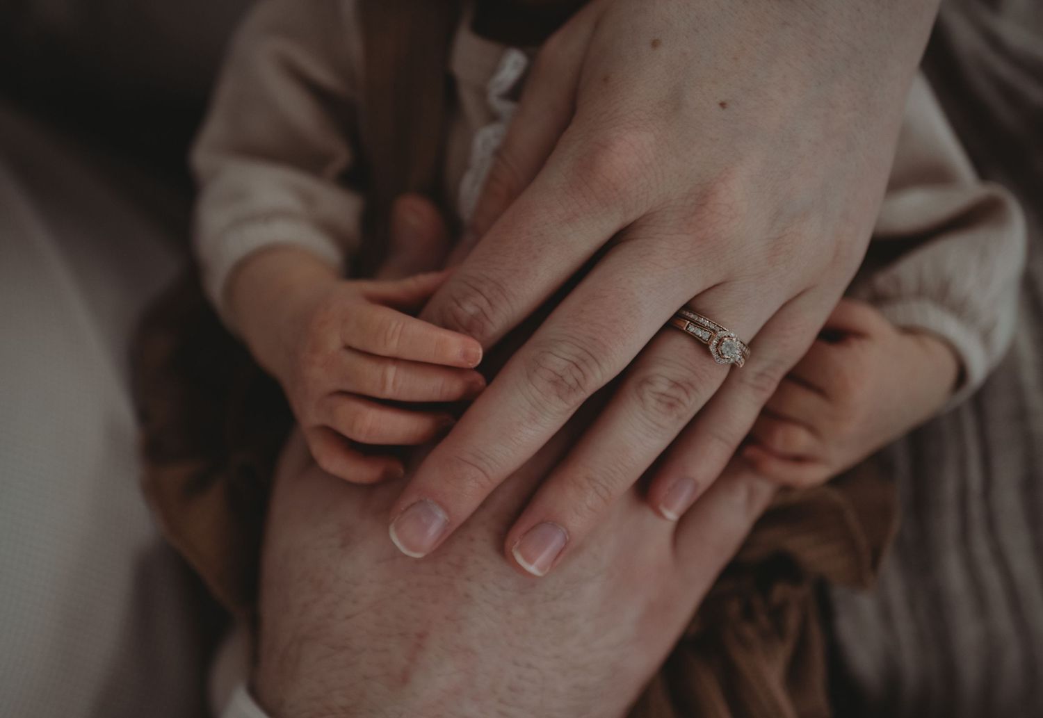 Close-up of a family's hands stacked together, showing a mother's delicate wedding ring.