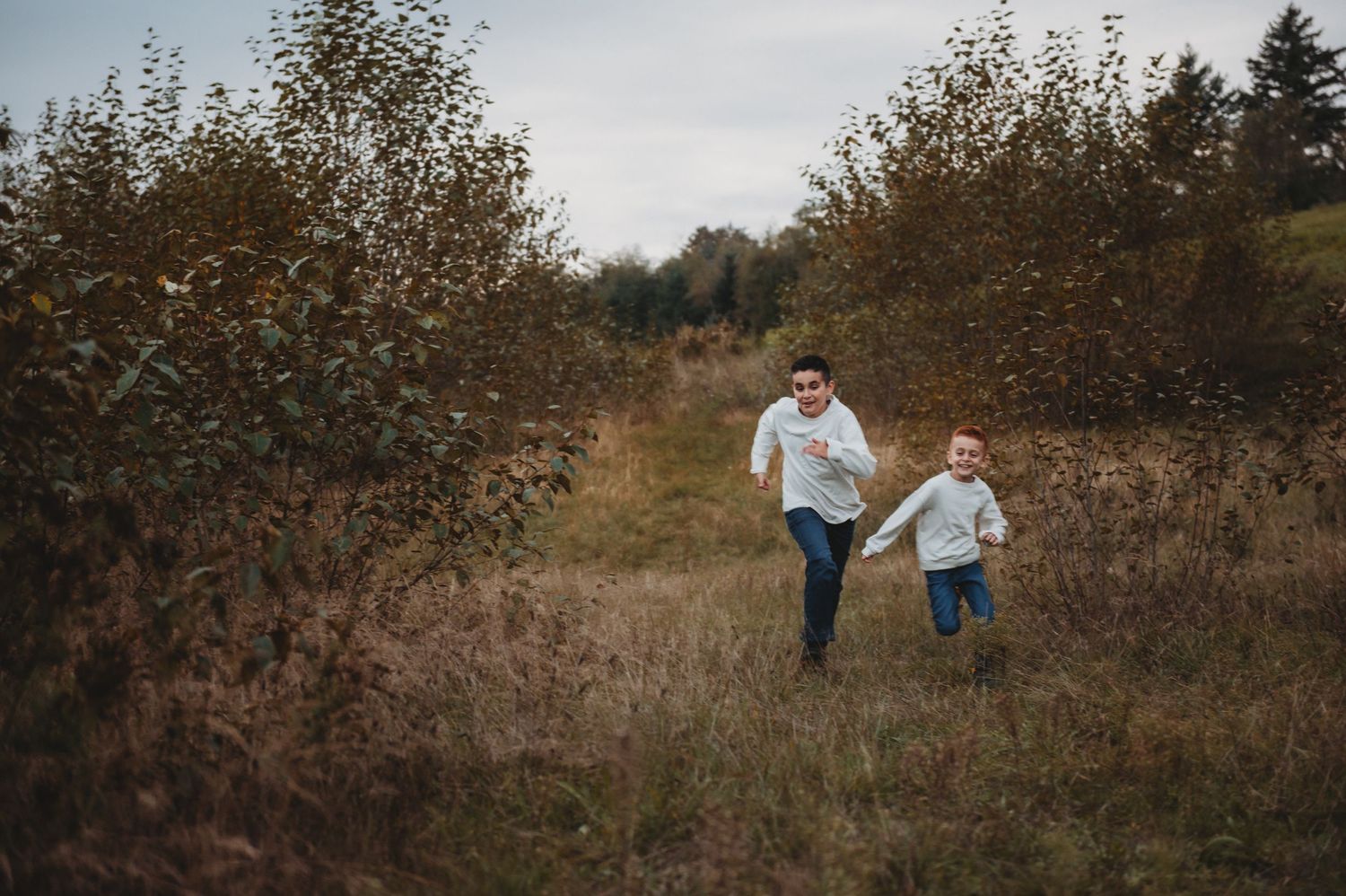 Father and young red-haired son running together through autumn meadow path outdoors.
