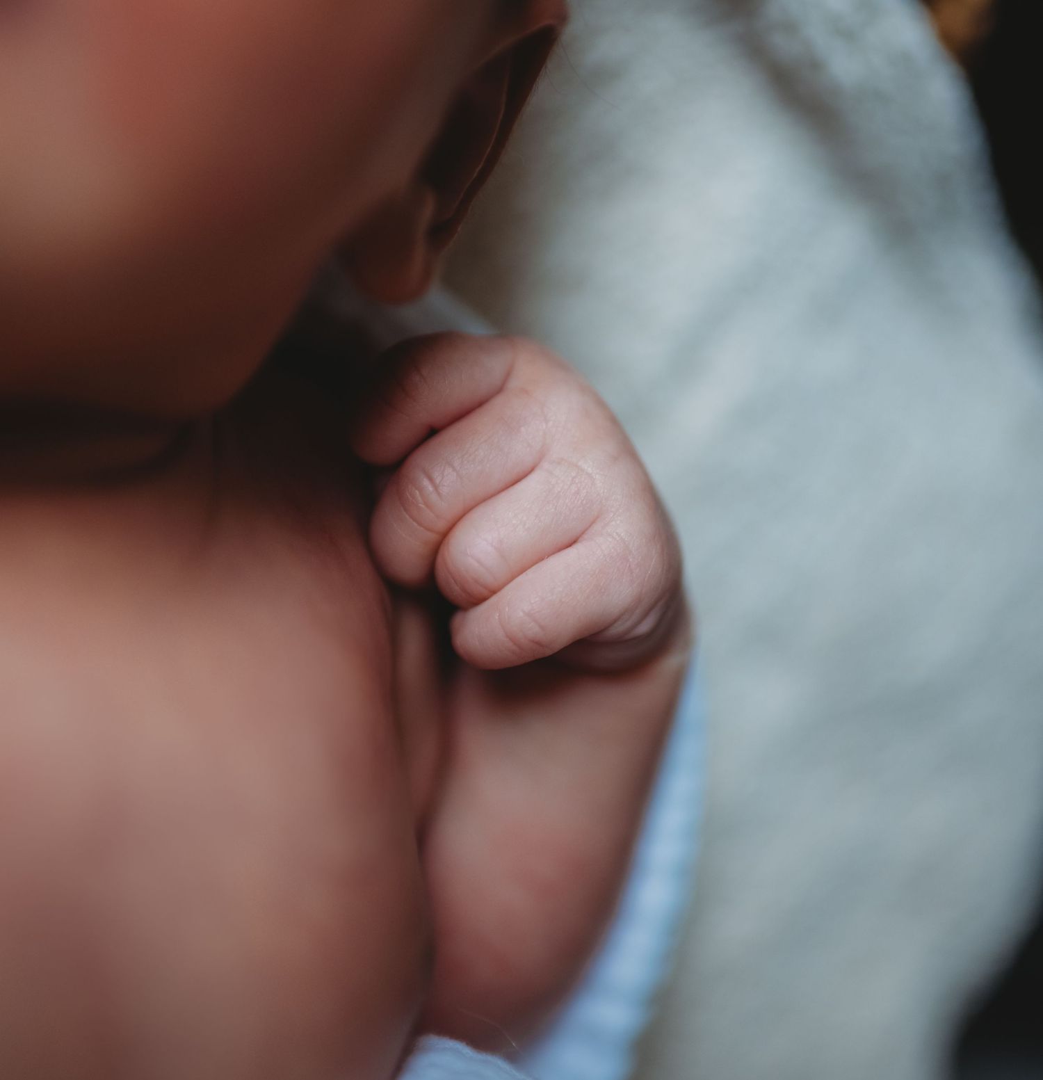 Close-up of a newborn baby tiny clenched fist resting on a soft white blanket.