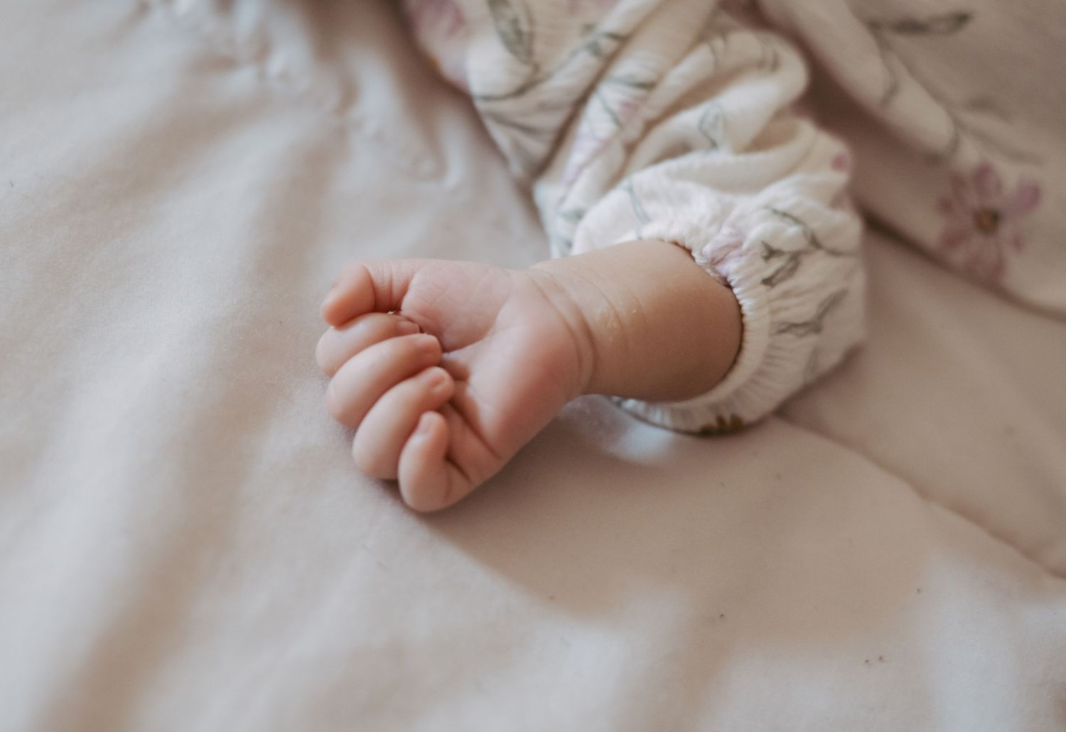 Close-up of tiny newborn baby hand in floral sleeve resting on white blanket.