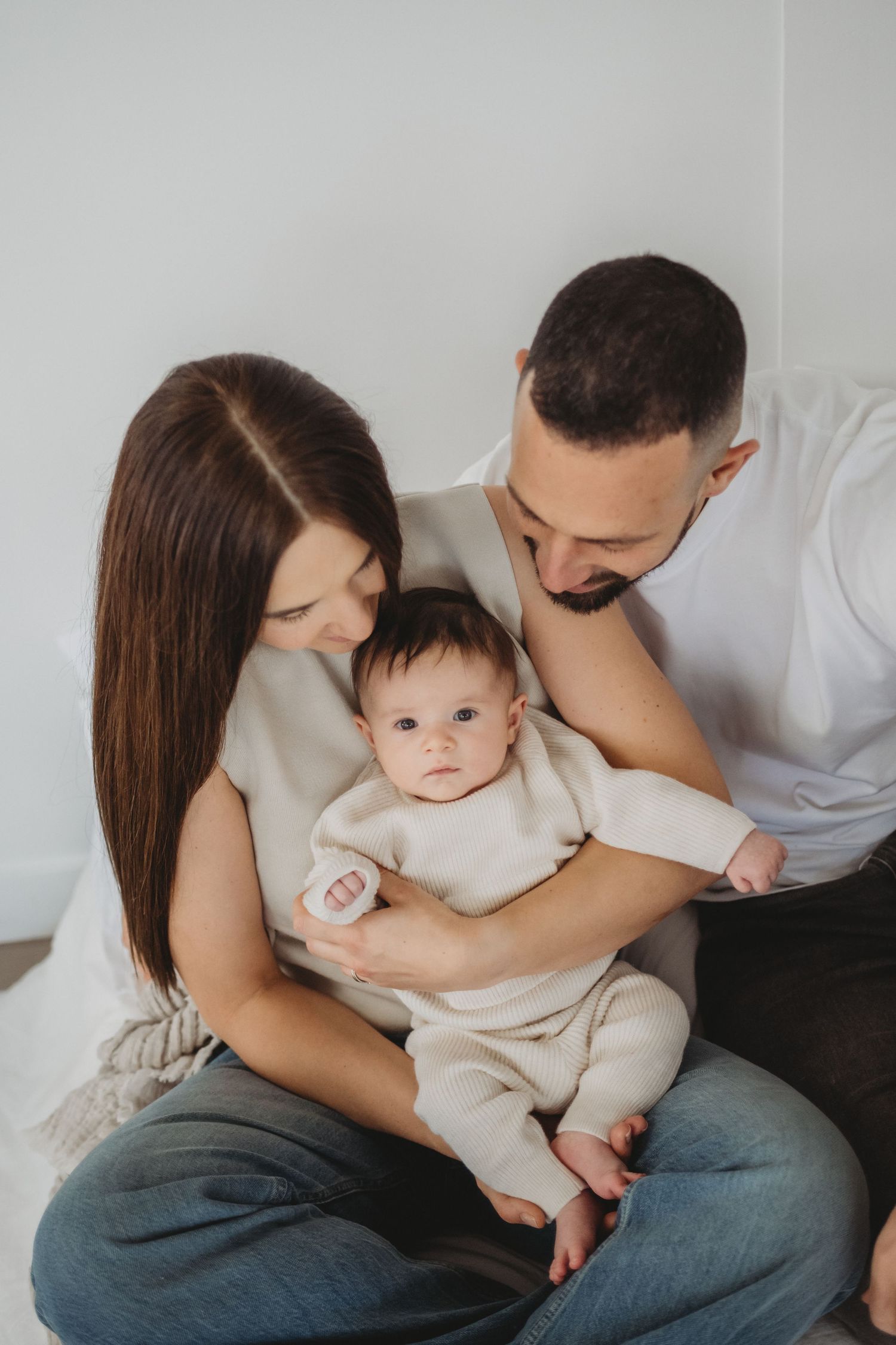 Loving parents holding infant in cream knit outfit against white studio background.