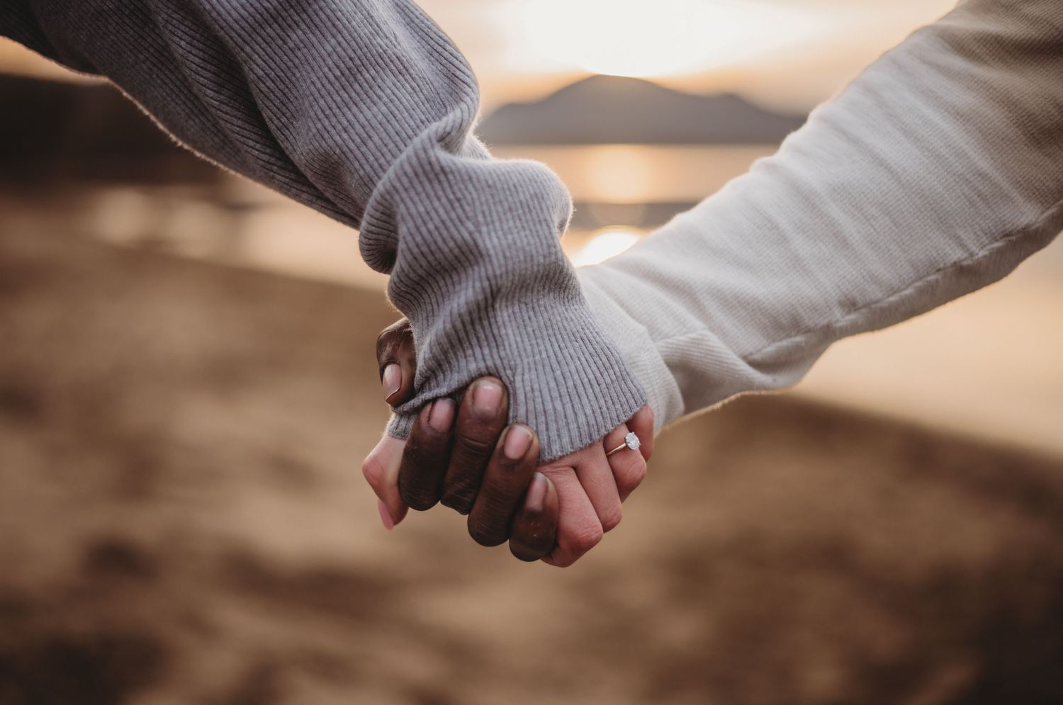 Close-up of an interracial couple holding hands, showcasing their contrasting skin tones at golden hour.