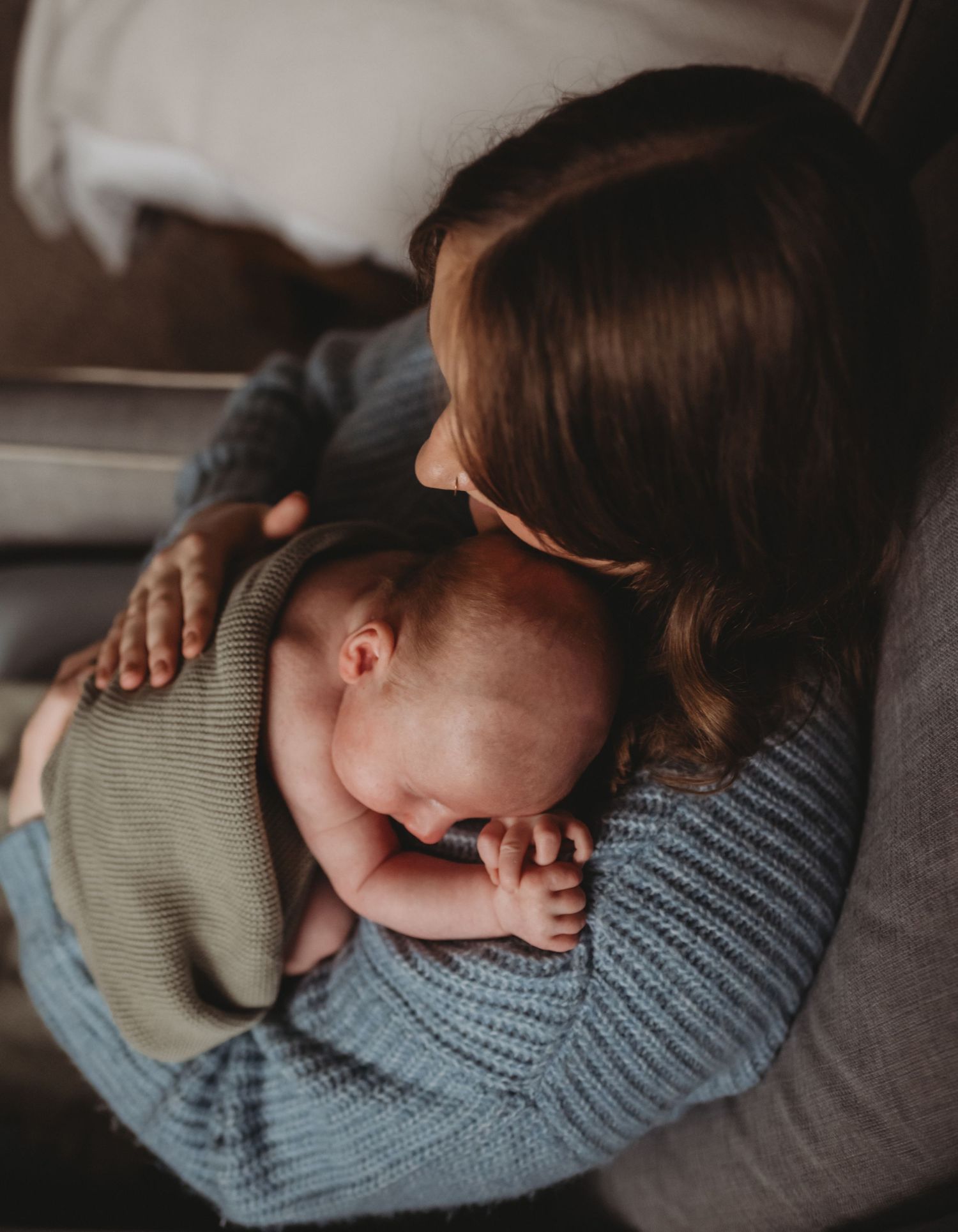 Mother in blue knit sweater lovingly holding sleeping newborn baby against her shoulder.