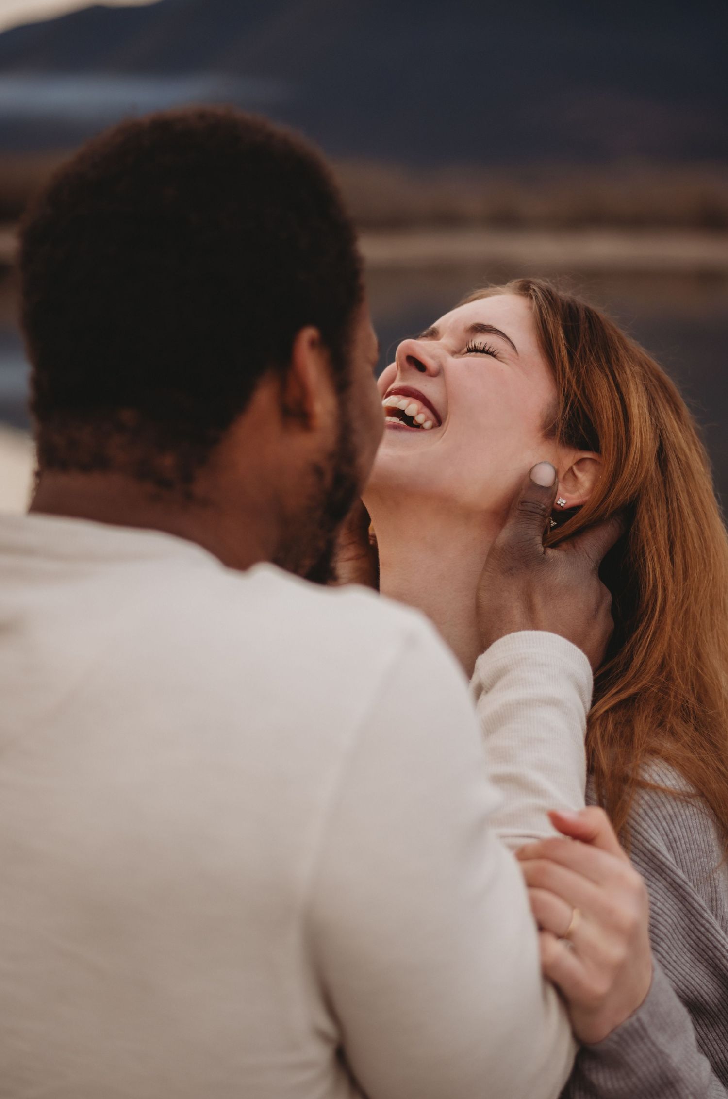 Joyful woman laughing while being held by her partner during outdoor couples photography.