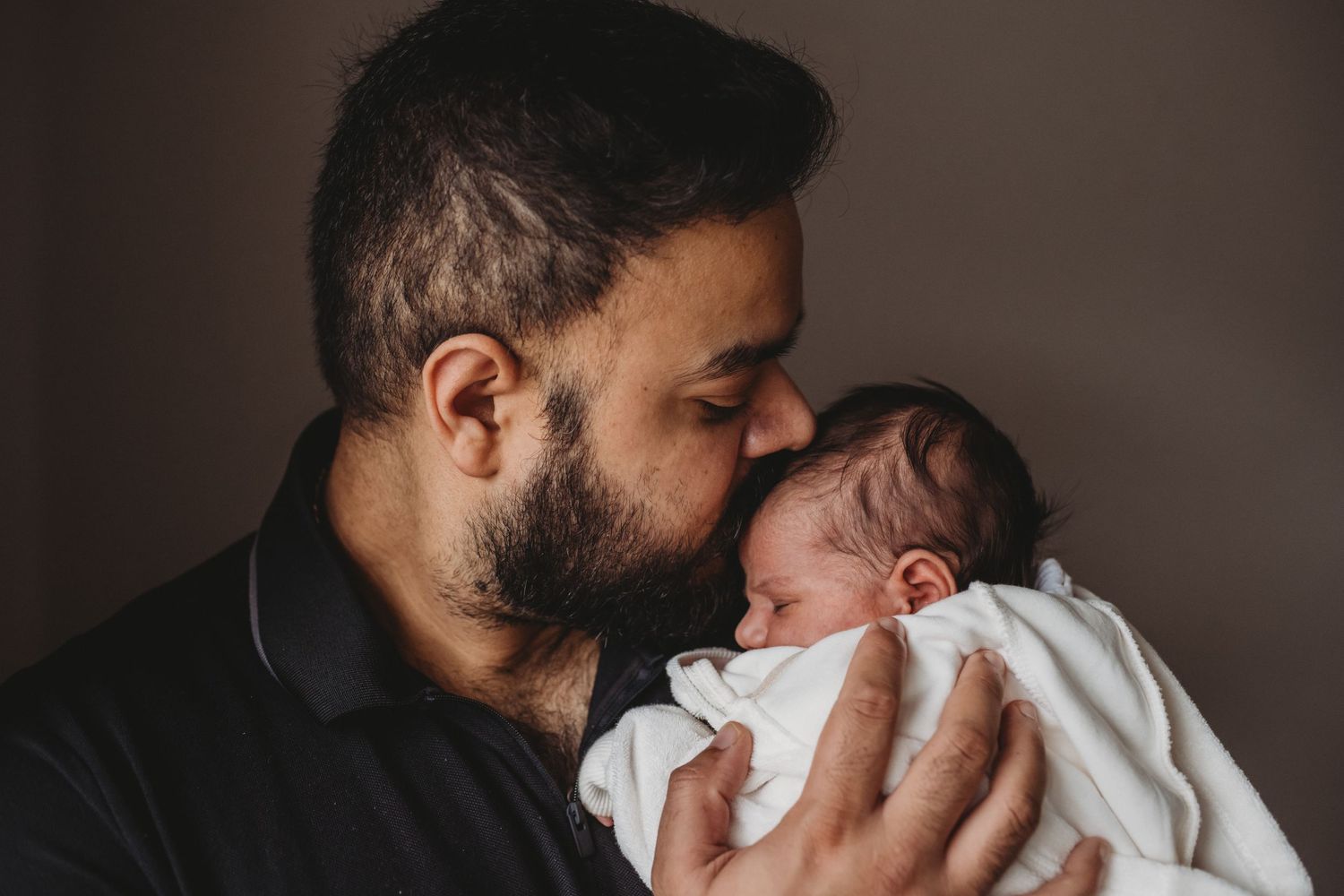 Loving father kissing his swaddled newborn baby wrapped in a white blanket.
