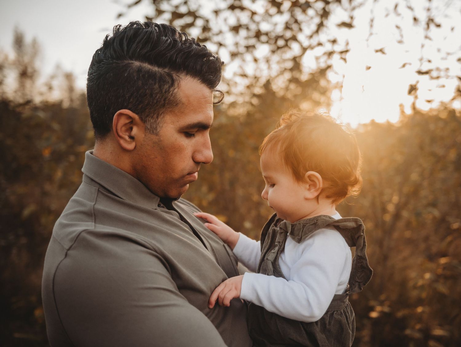 Father tenderly holding baby in warm golden sunset light.