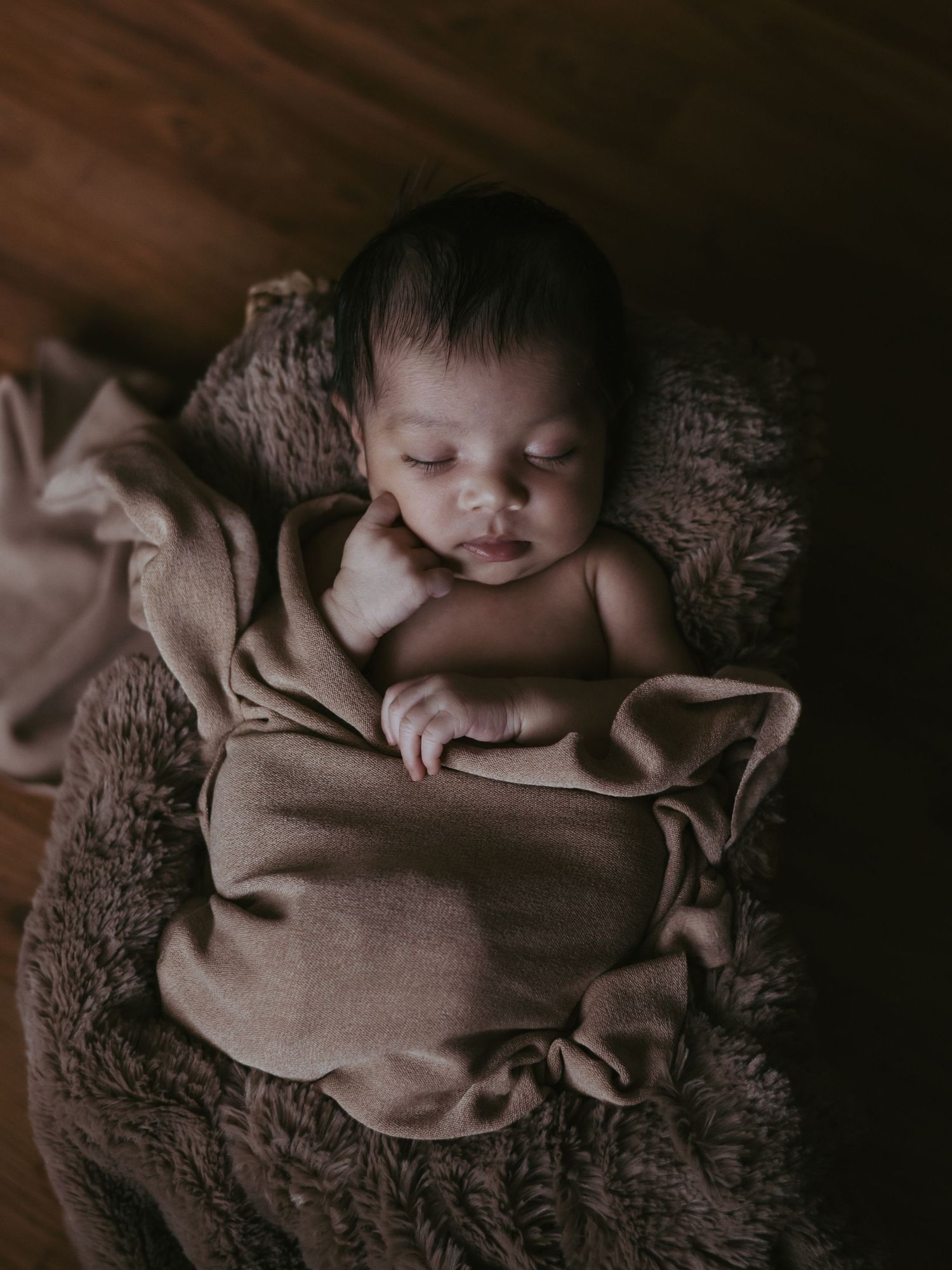 A peaceful newborn baby sleeps wrapped in a soft brown blanket in a cozy basket.