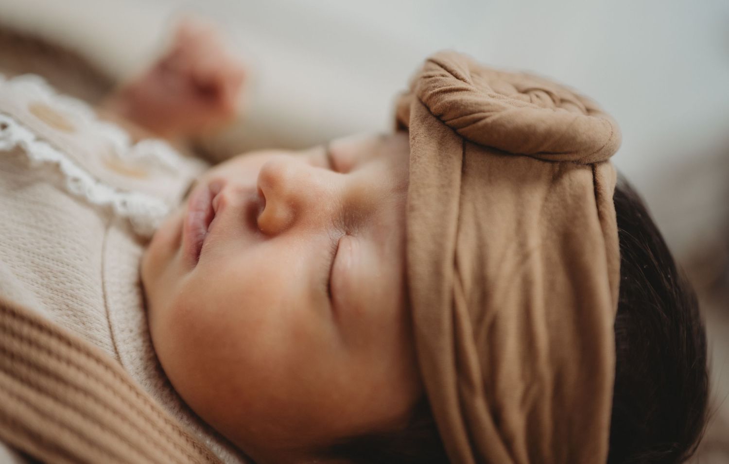 Peaceful sleeping newborn baby wearing a soft tan headband wrap during a newborn photo session.