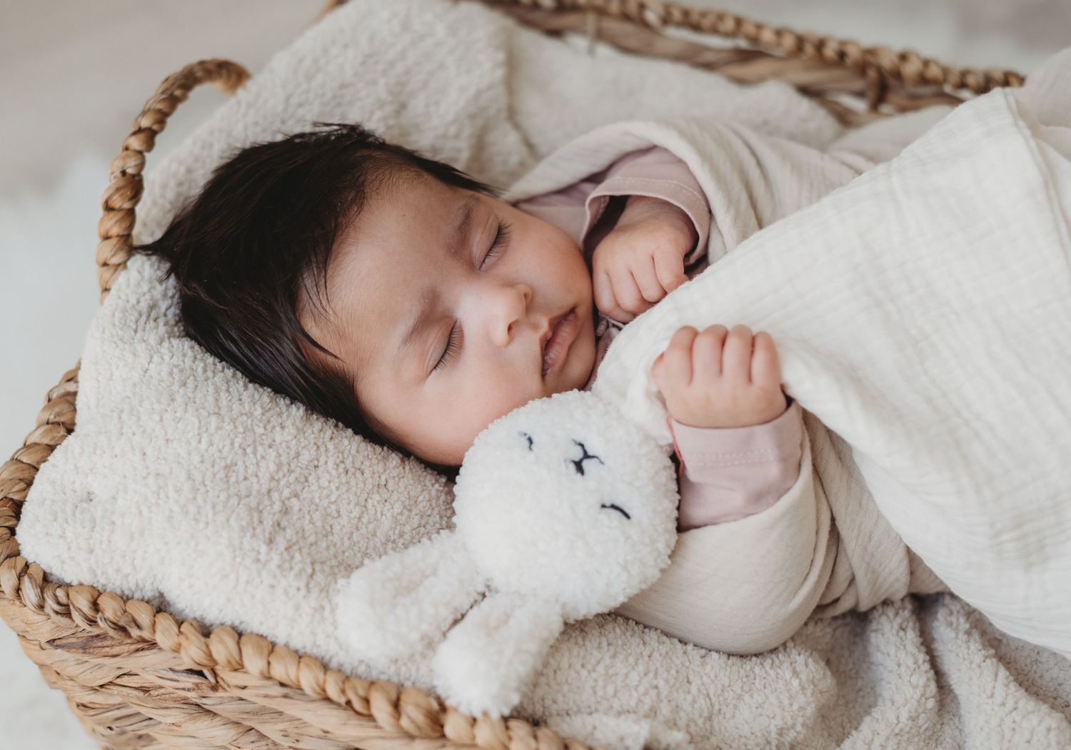 Peaceful newborn baby sleeping in wicker basket with soft bunny stuffed animal toy.