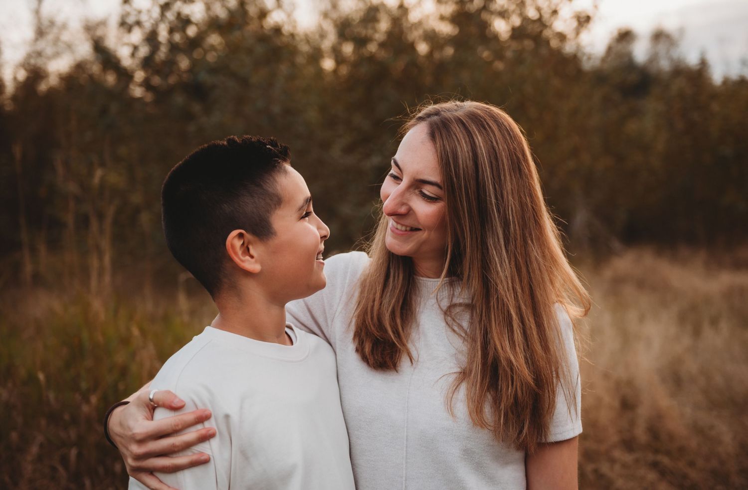 Mother and preteen son smiling at each other in warm golden outdoor setting.