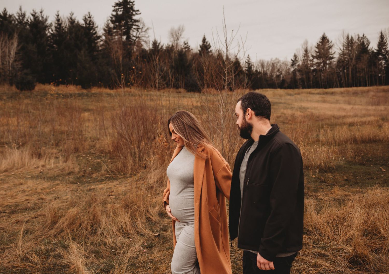 Pregnant couple walking hand-in-hand through a golden autumn field at twilight.