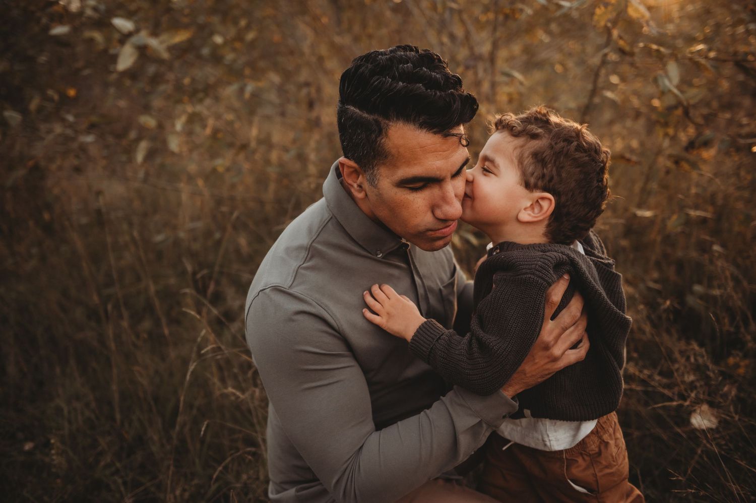 Young boy giving his father a kiss on the cheek in a warm golden autumn field.