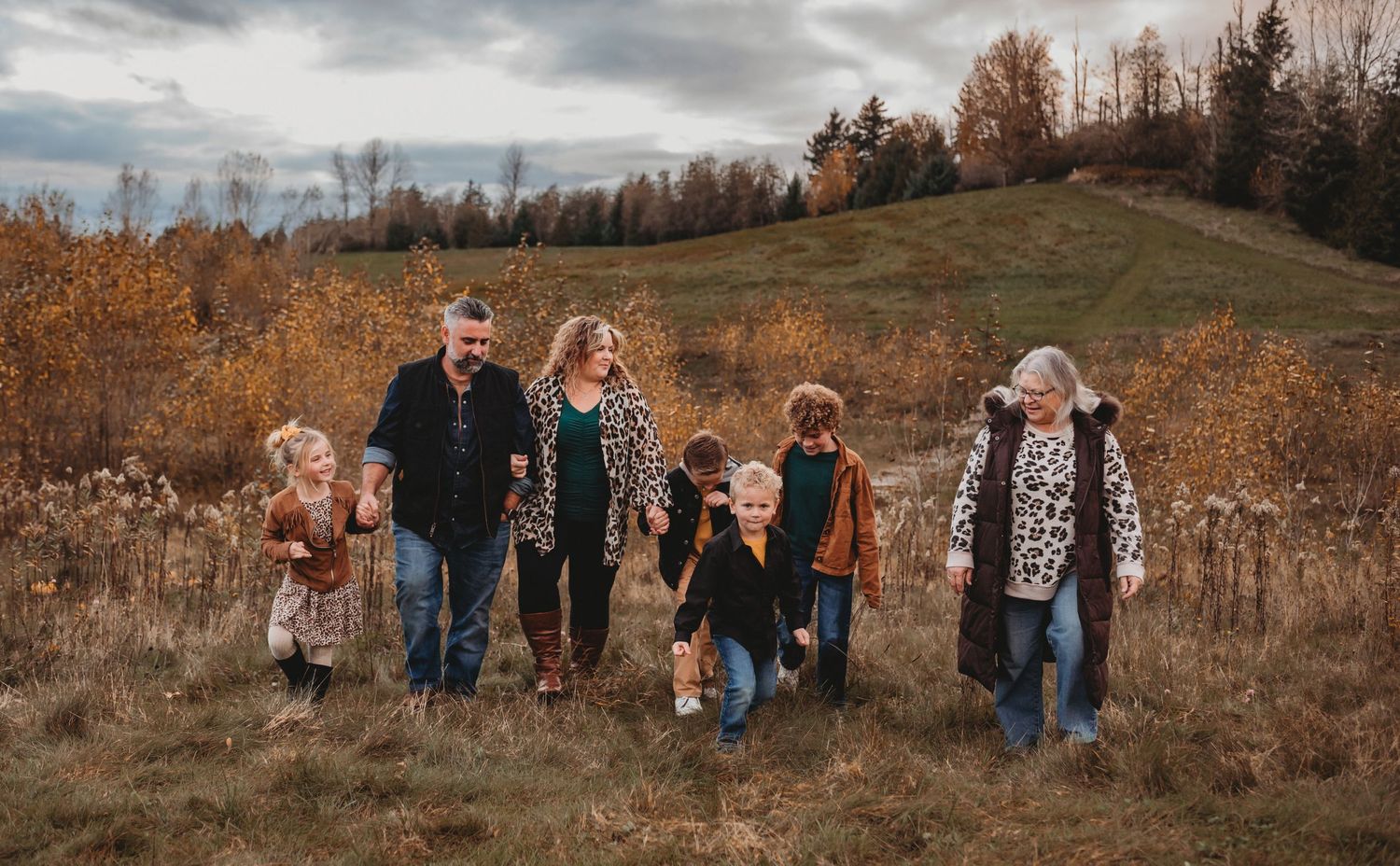 A large multigenerational family holds hands walking through a beautiful golden autumn landscape.