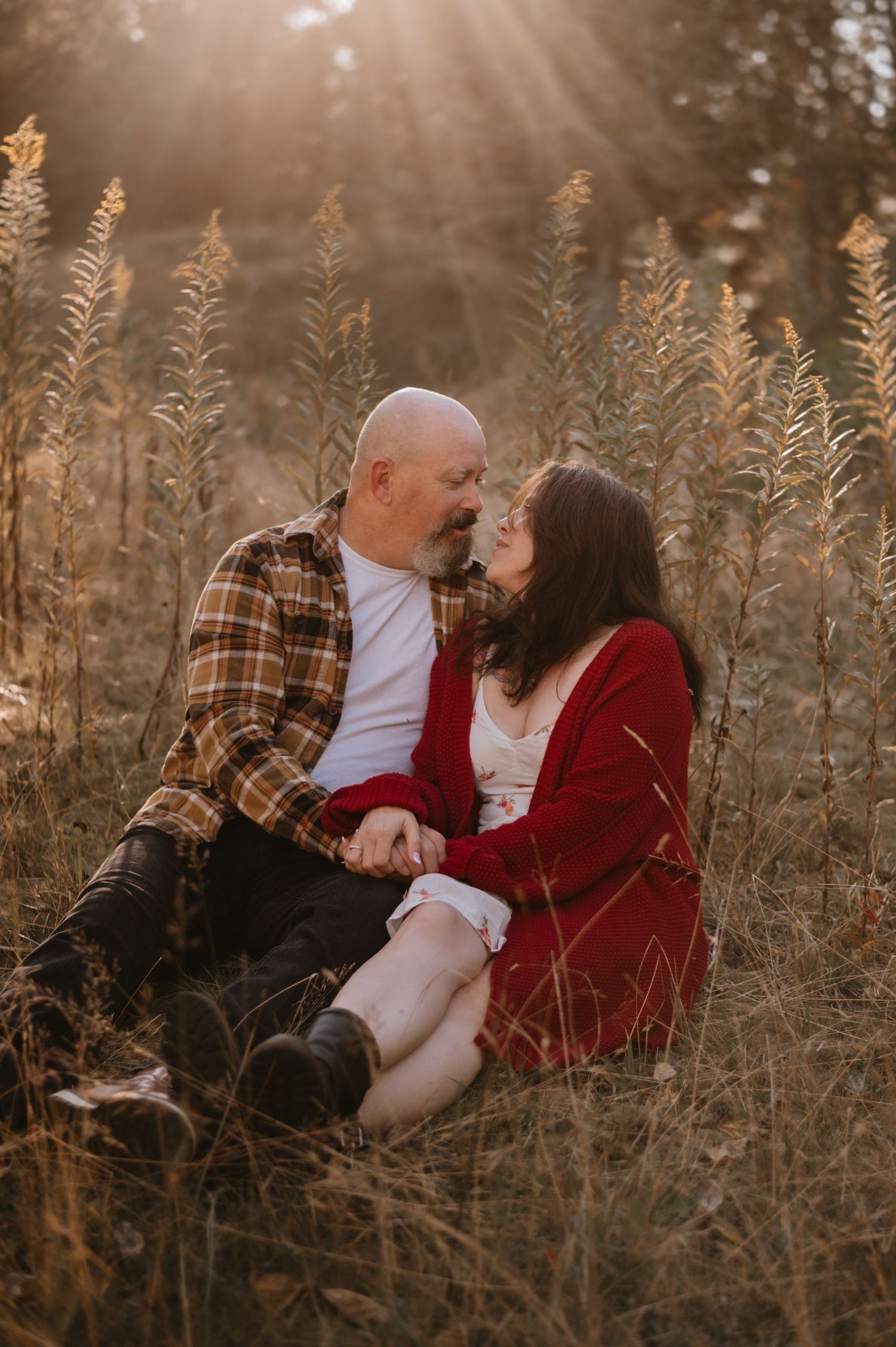 Couple sharing a romantic moment sitting in a sunlit golden field at sunset.