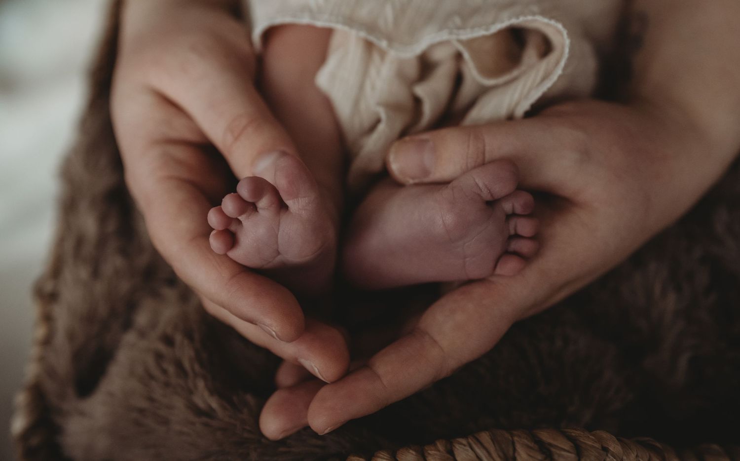 Parent hands cradling tiny newborn baby feet in a heart shape, close-up newborn photography.