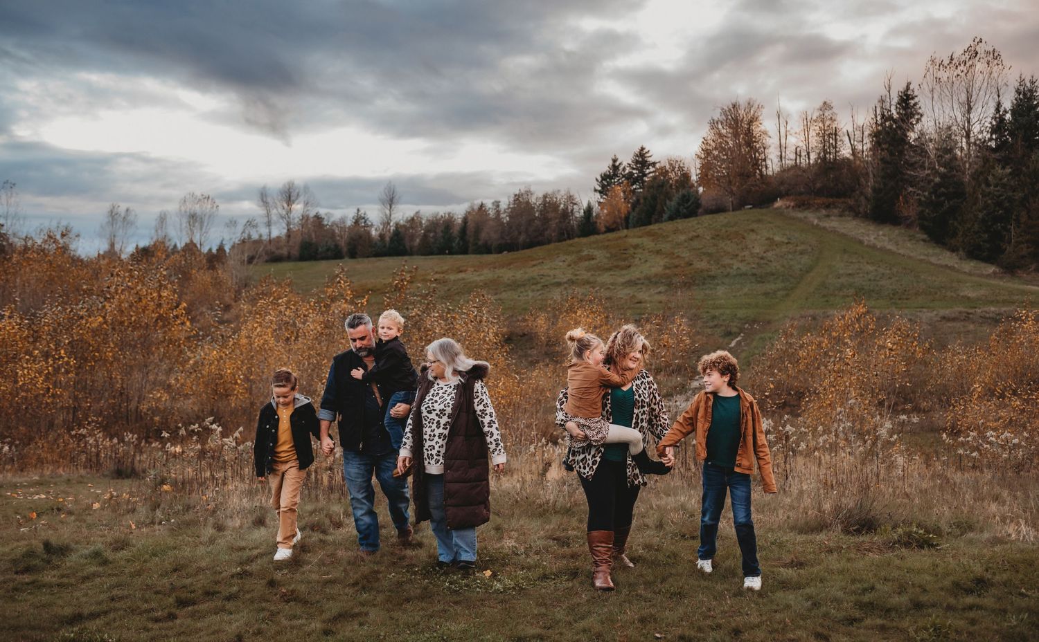 A multigenerational family strolls together through a scenic autumn field with golden foliage.