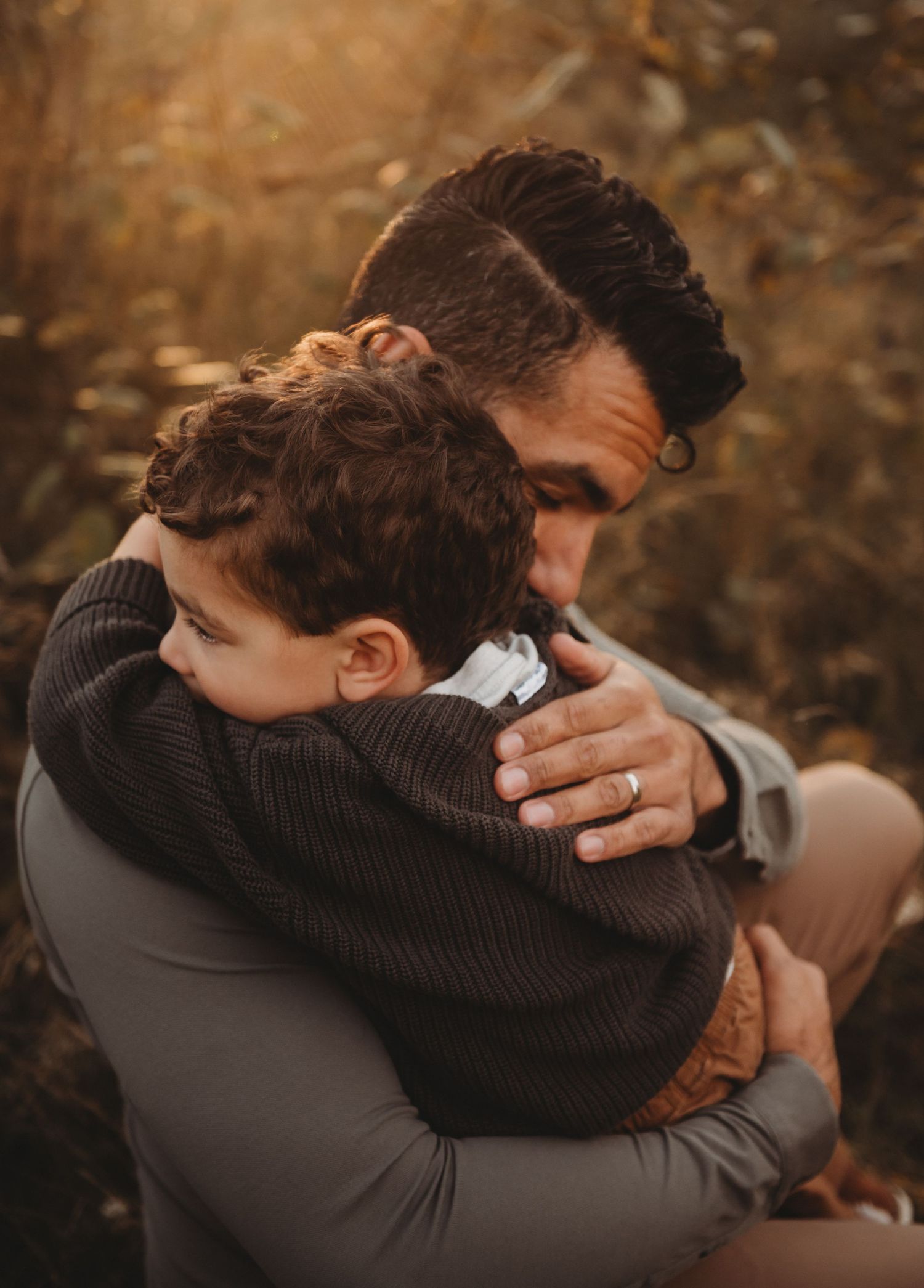 Father and young son sharing a tender hug in a warm golden autumn outdoor setting.