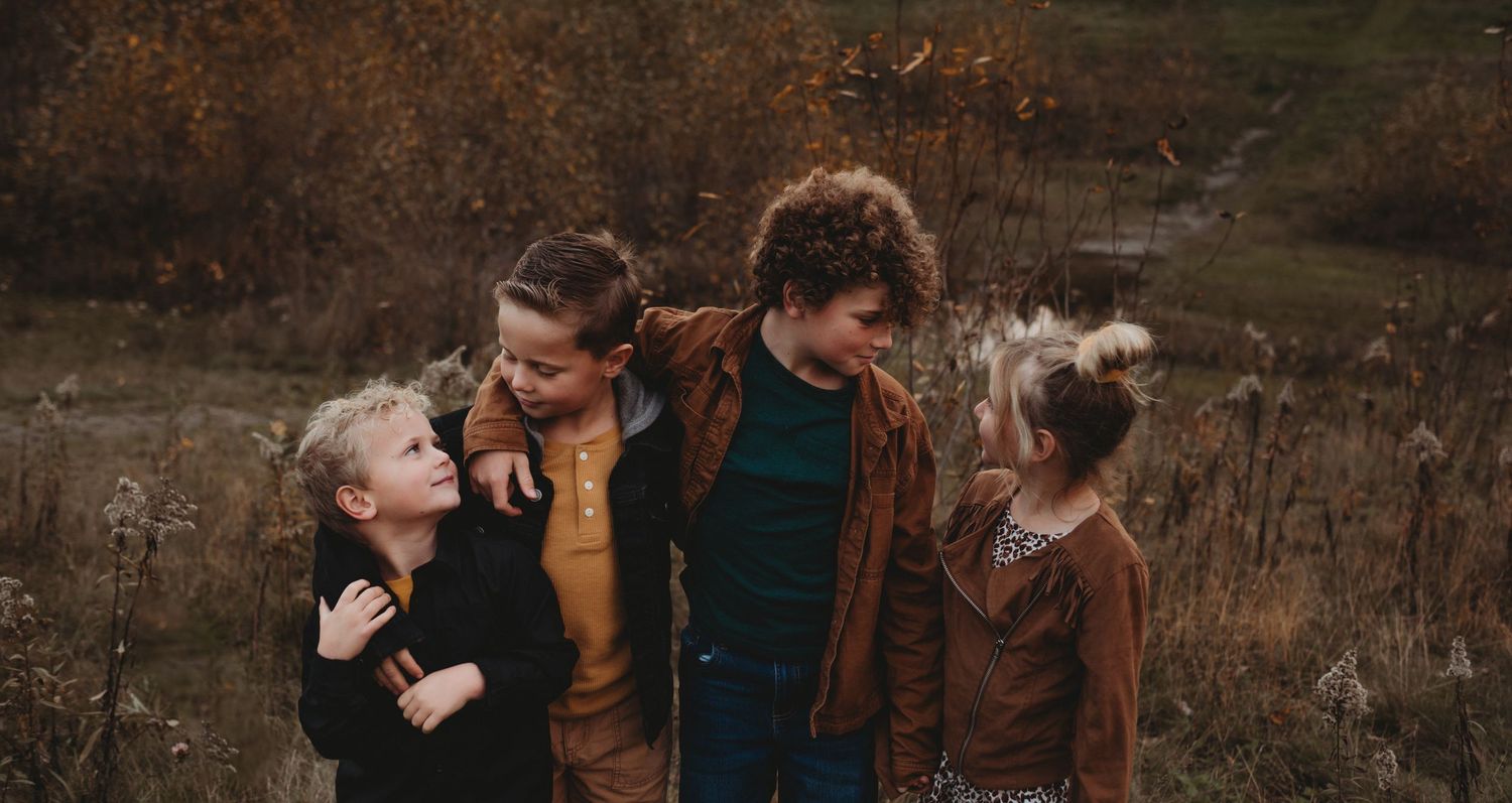Four children laughing and embracing together in an autumn field during a family photo session.