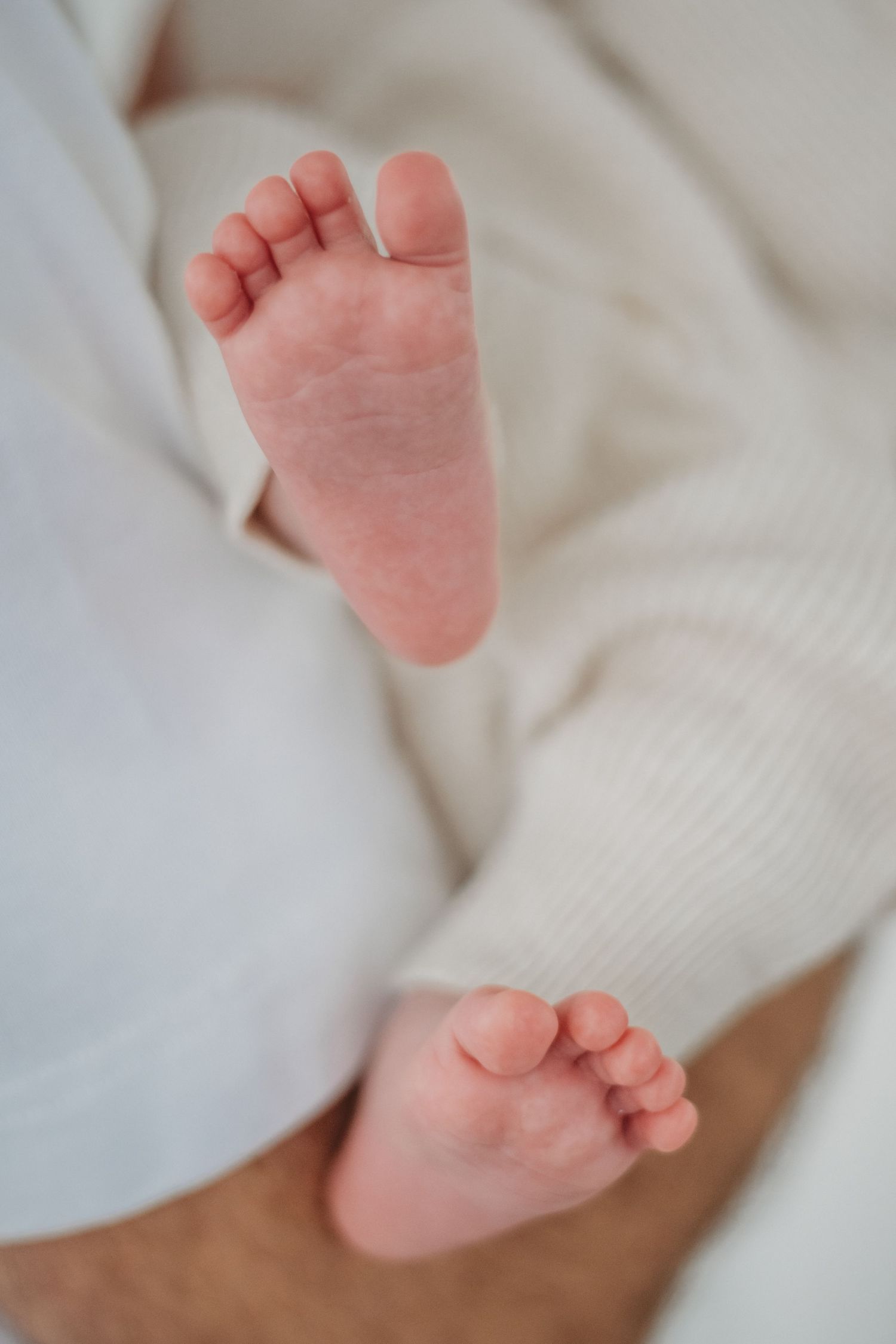 Close-up of tiny newborn baby feet in cream white knit outfit.