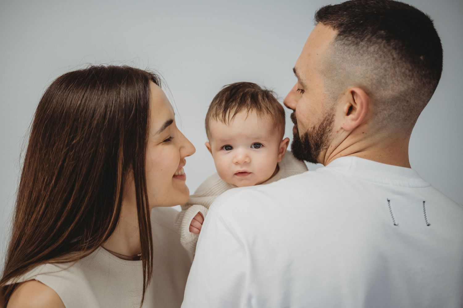 Happy young family with mother and bearded father admiring their cute baby.