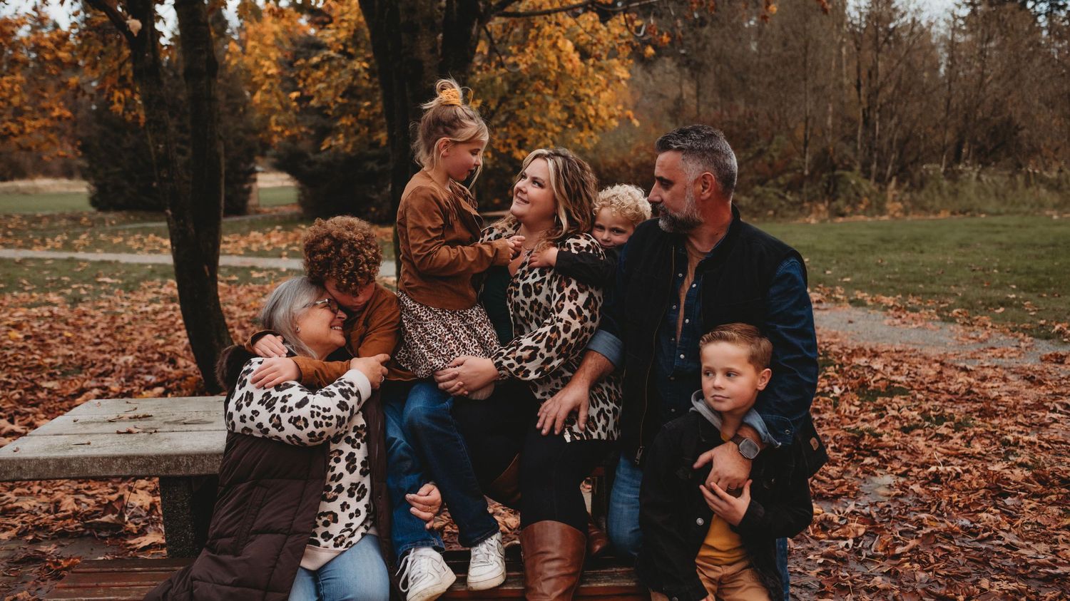 A happy family of six sits together on a bench surrounded by colorful autumn foliage.