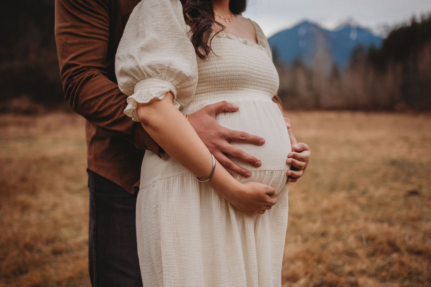 Close-up of couple cradling pregnant belly during outdoor maternity photography session in a field.