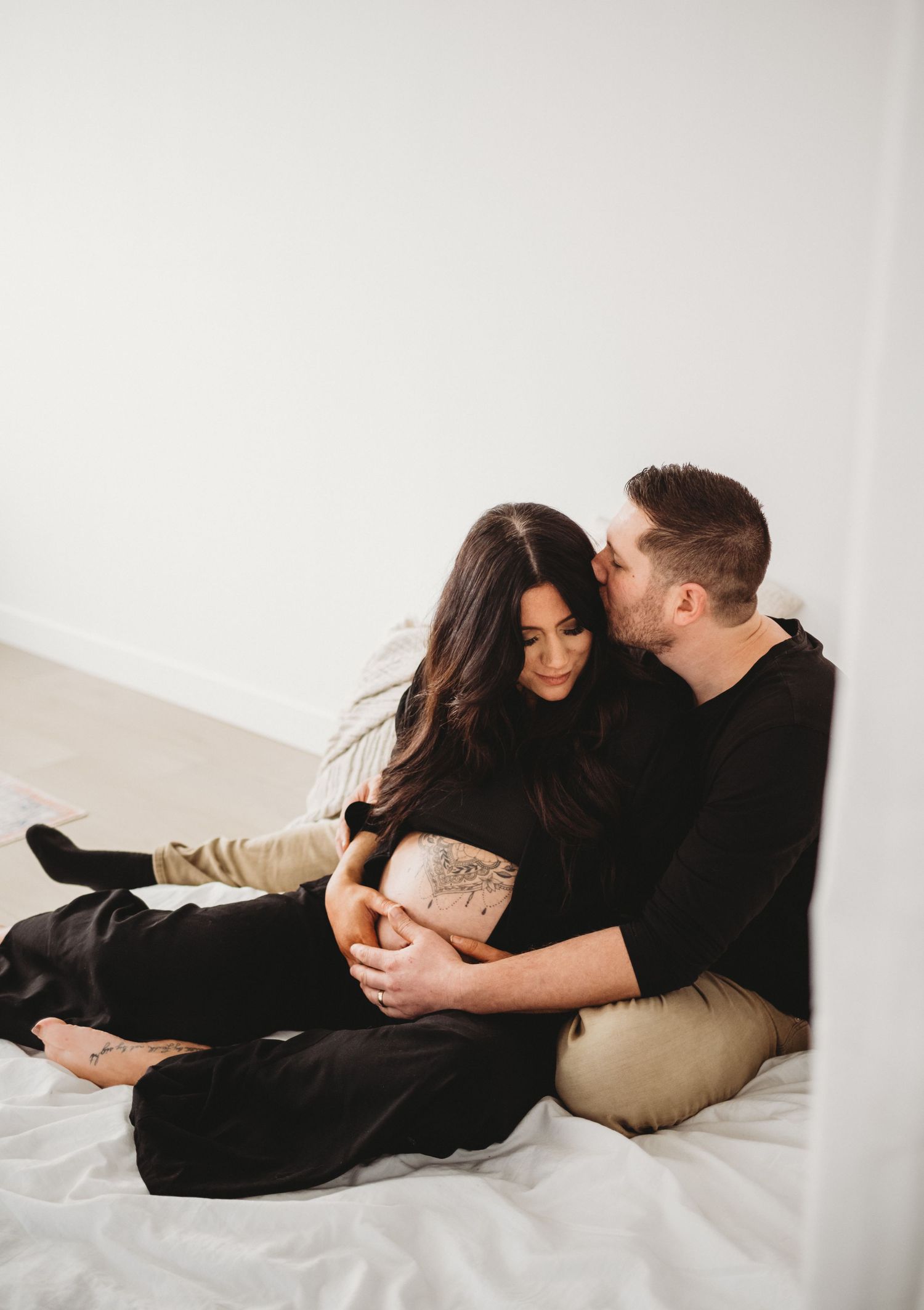 Couple sitting on floor embracing pregnant belly during maternity session.