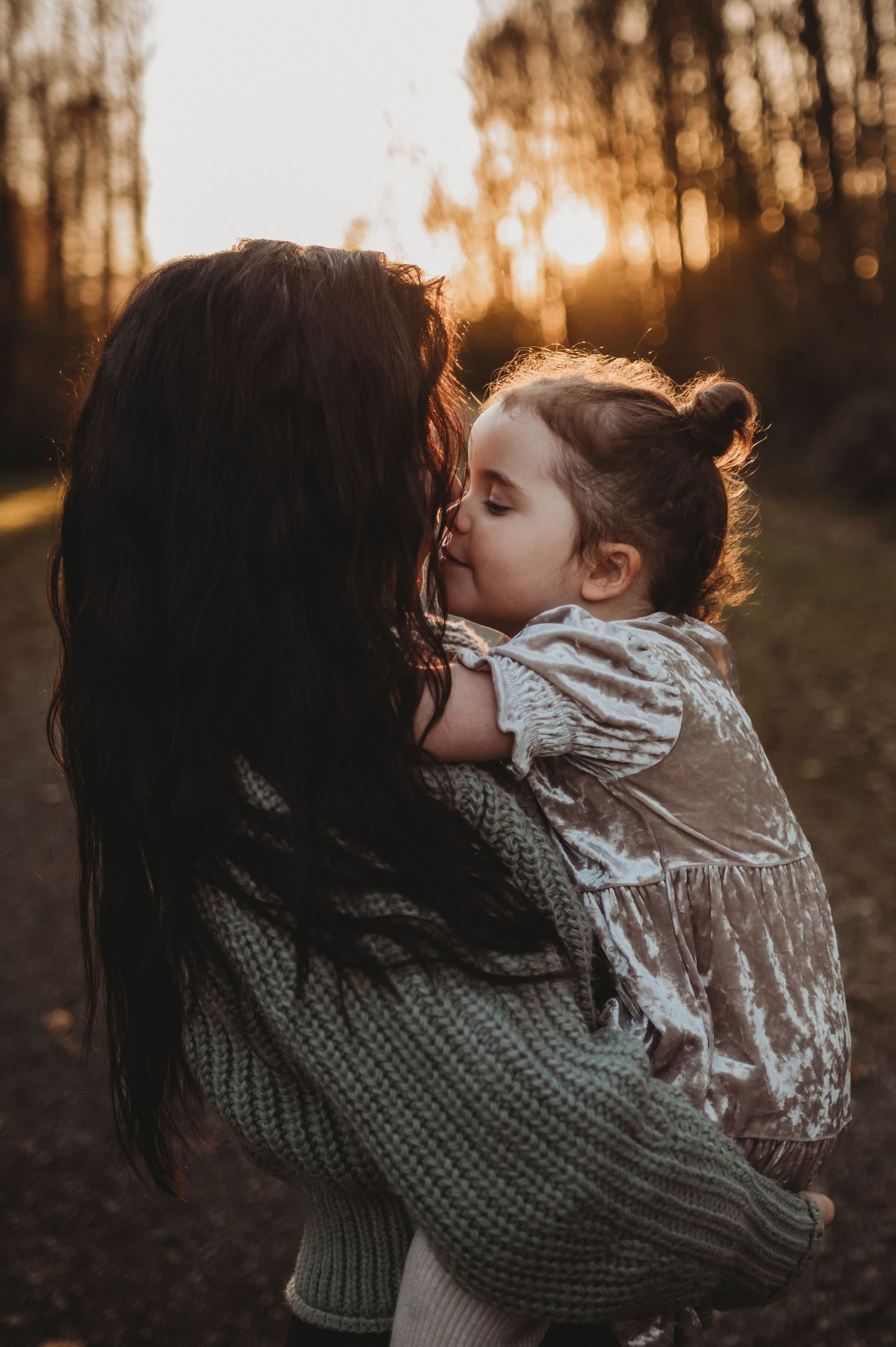 Tender moment of young child kissing mother on cheek at golden sunset in autumn forest setting.