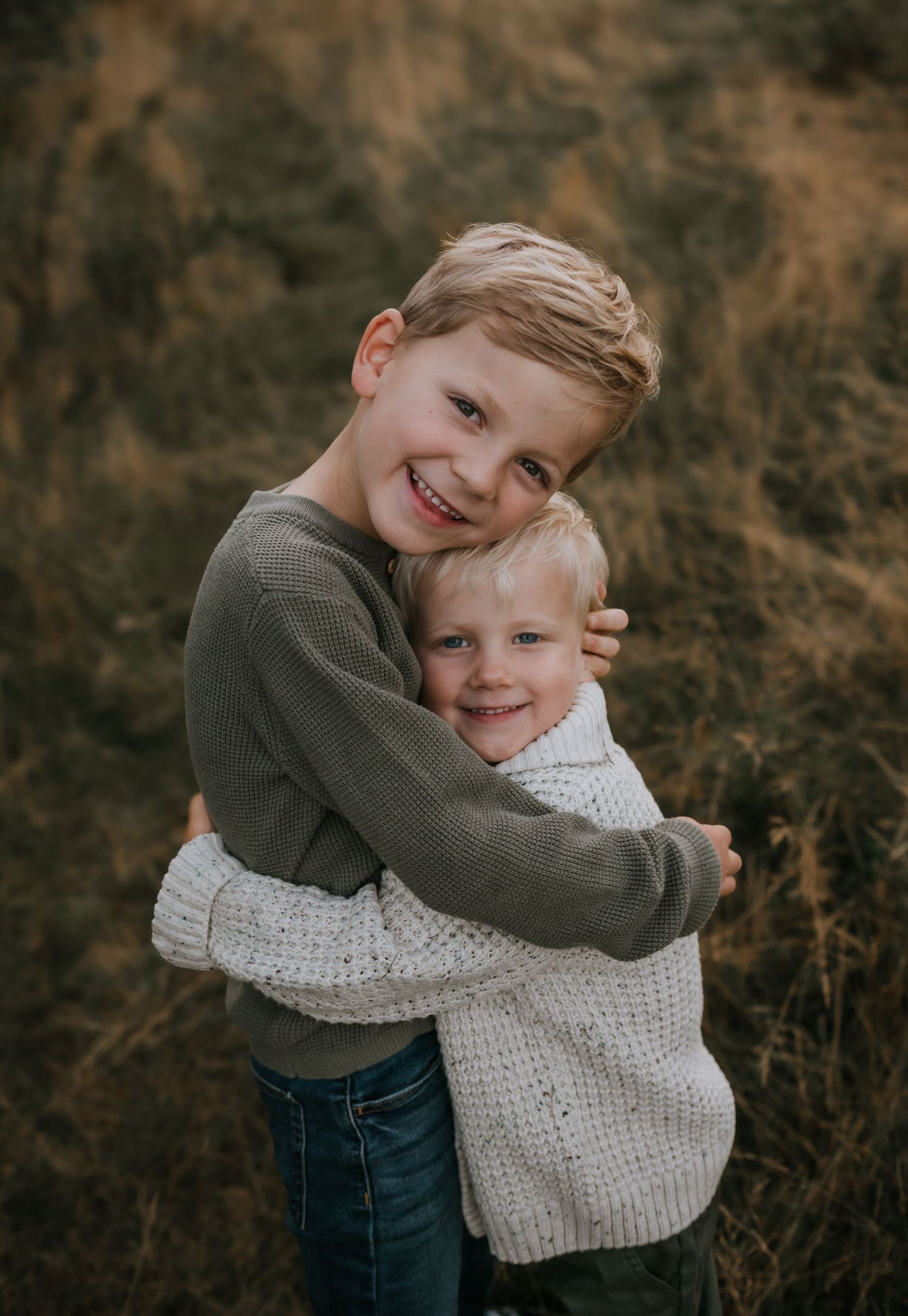 Two young brothers hugging and smiling in an autumn field during a family photo session.