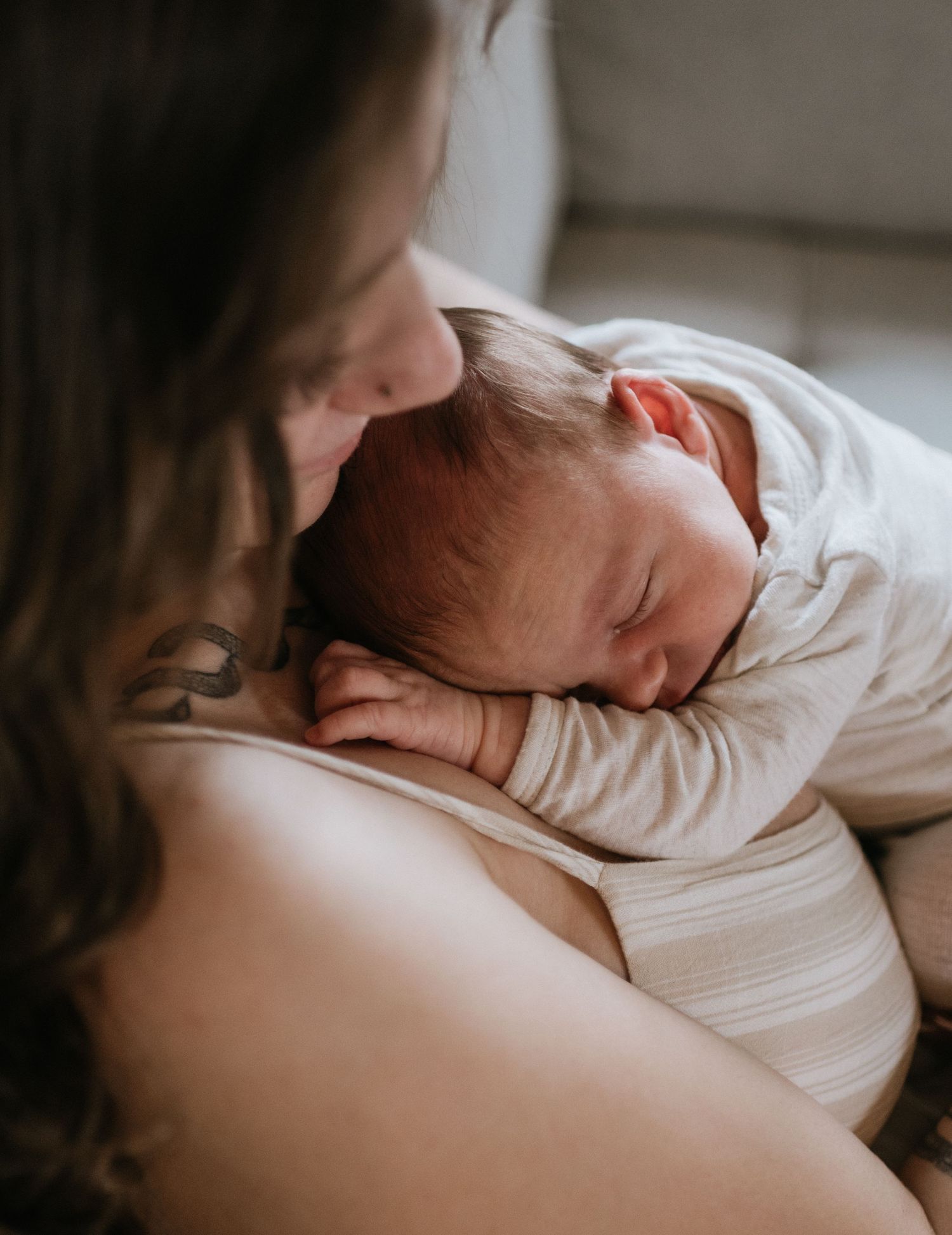 Mother tenderly gazing at sleeping newborn baby resting on her chest.