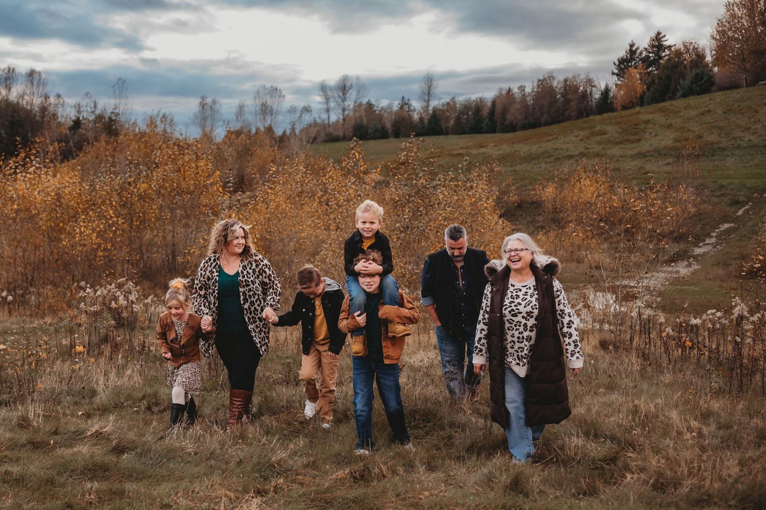 A multigenerational family walks joyfully through an autumn field with colorful fall foliage.
