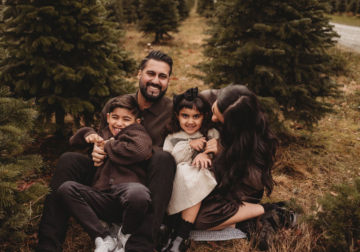 A joyful family of four laughs together among evergreen trees in a festive outdoor setting.