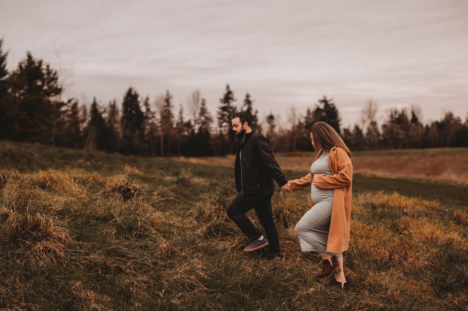 Couple holding hands in golden field during outdoor maternity session.