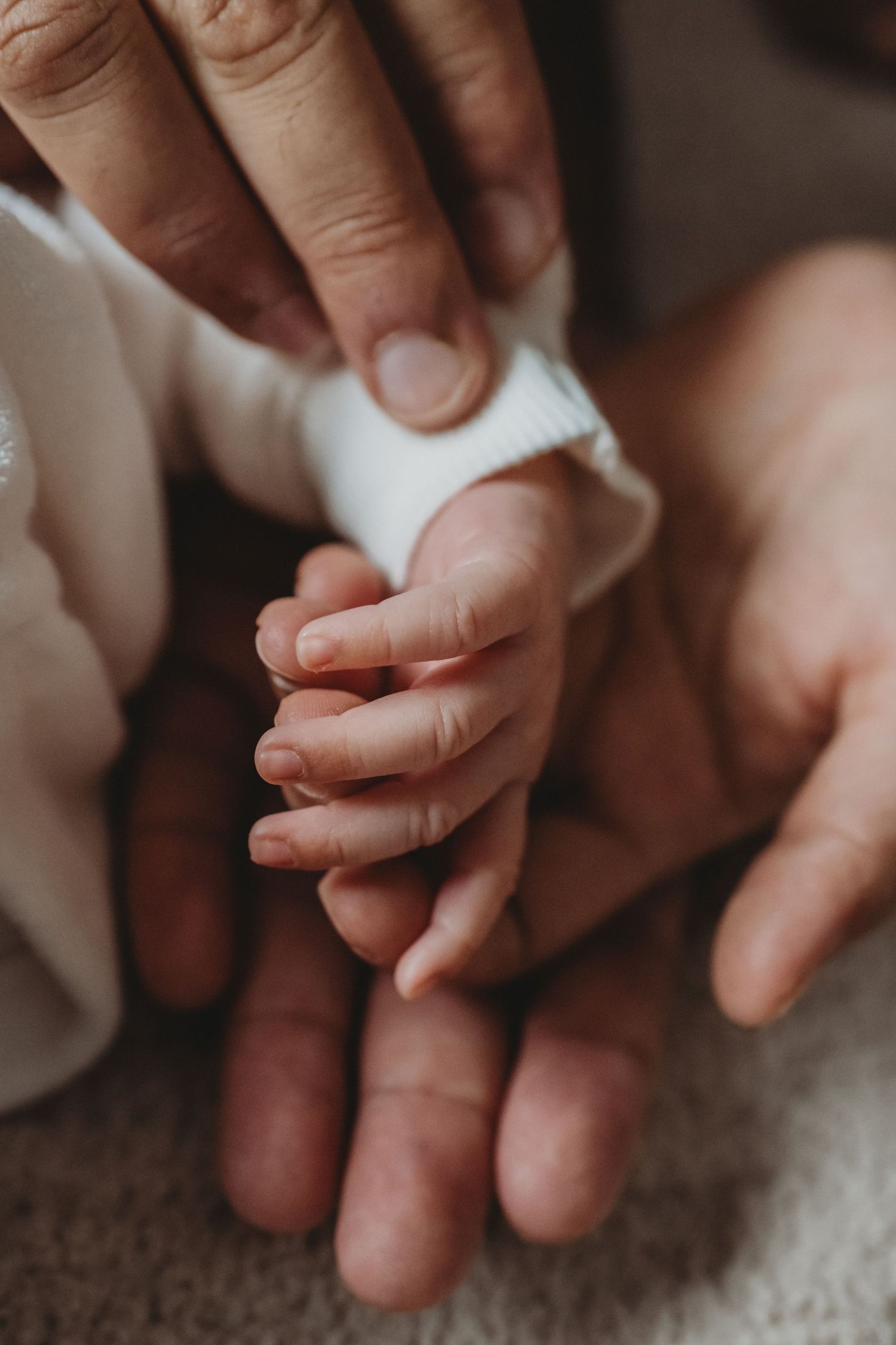 Newborn baby tiny hand grasping parent's finger, close-up of infant and adult hands bonding moment.
